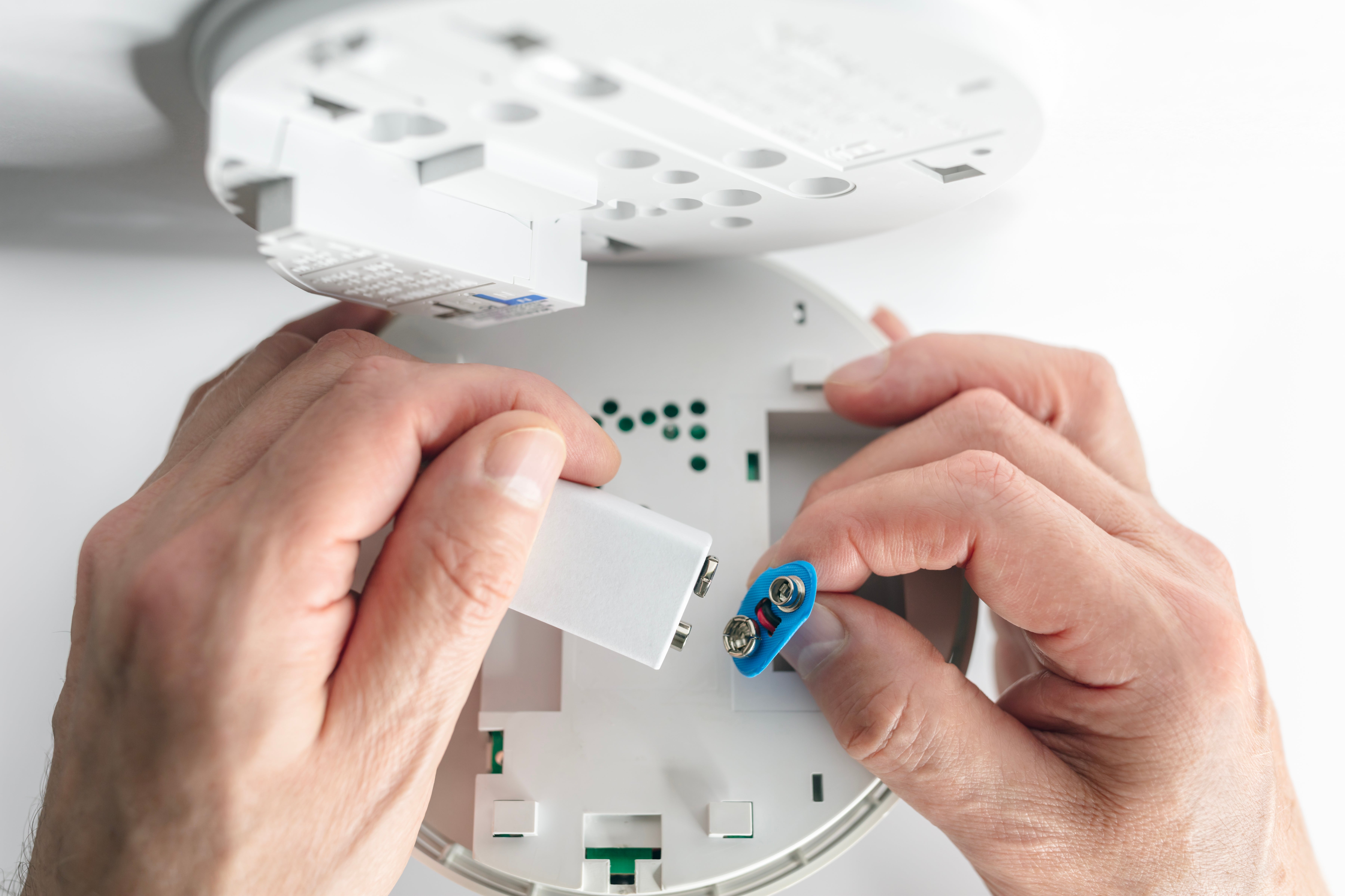 Hands installing a battery into a smoke detector