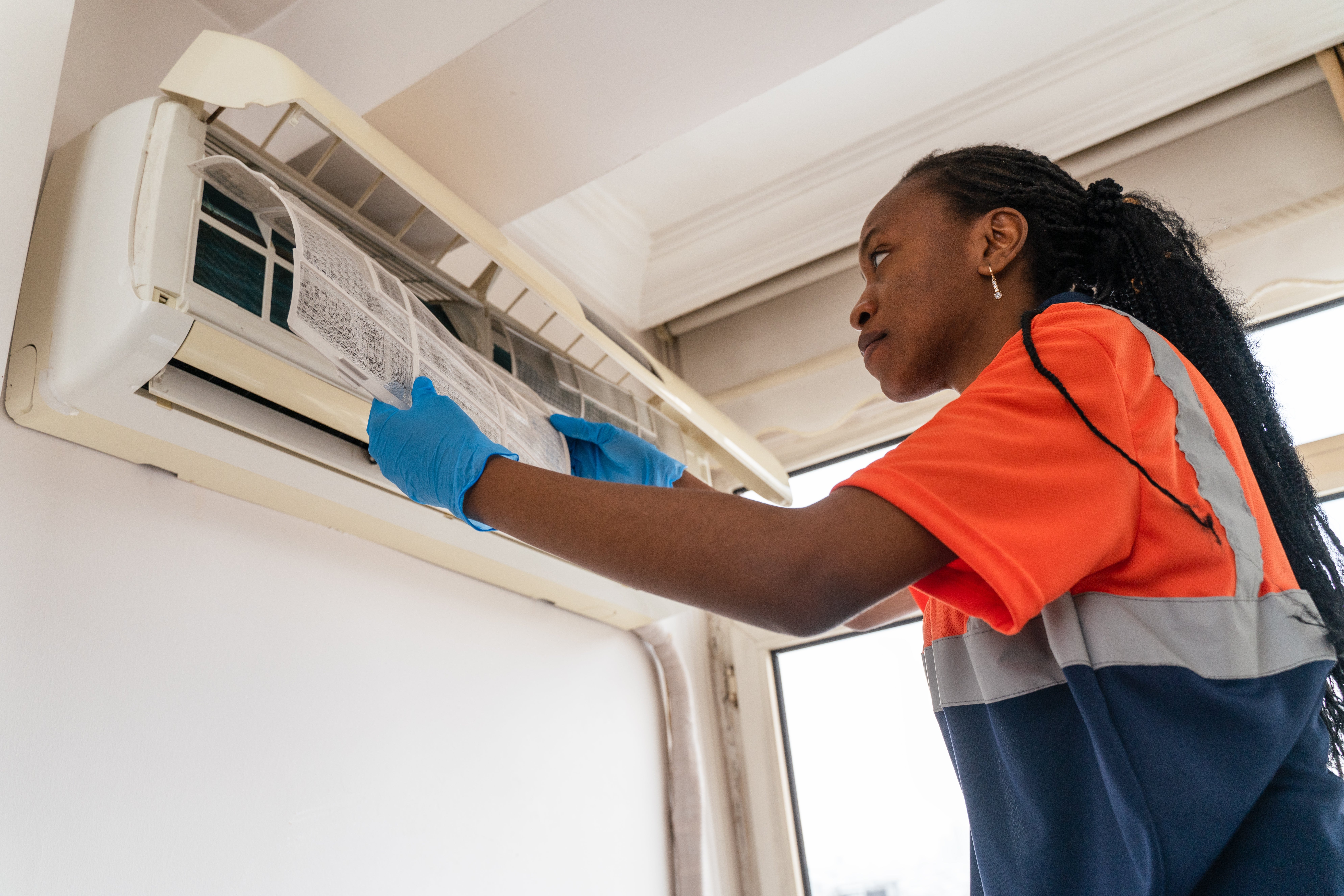 A technician wearing protective gloves inspects an air conditioning unit, adjusting the filter with focus and precision