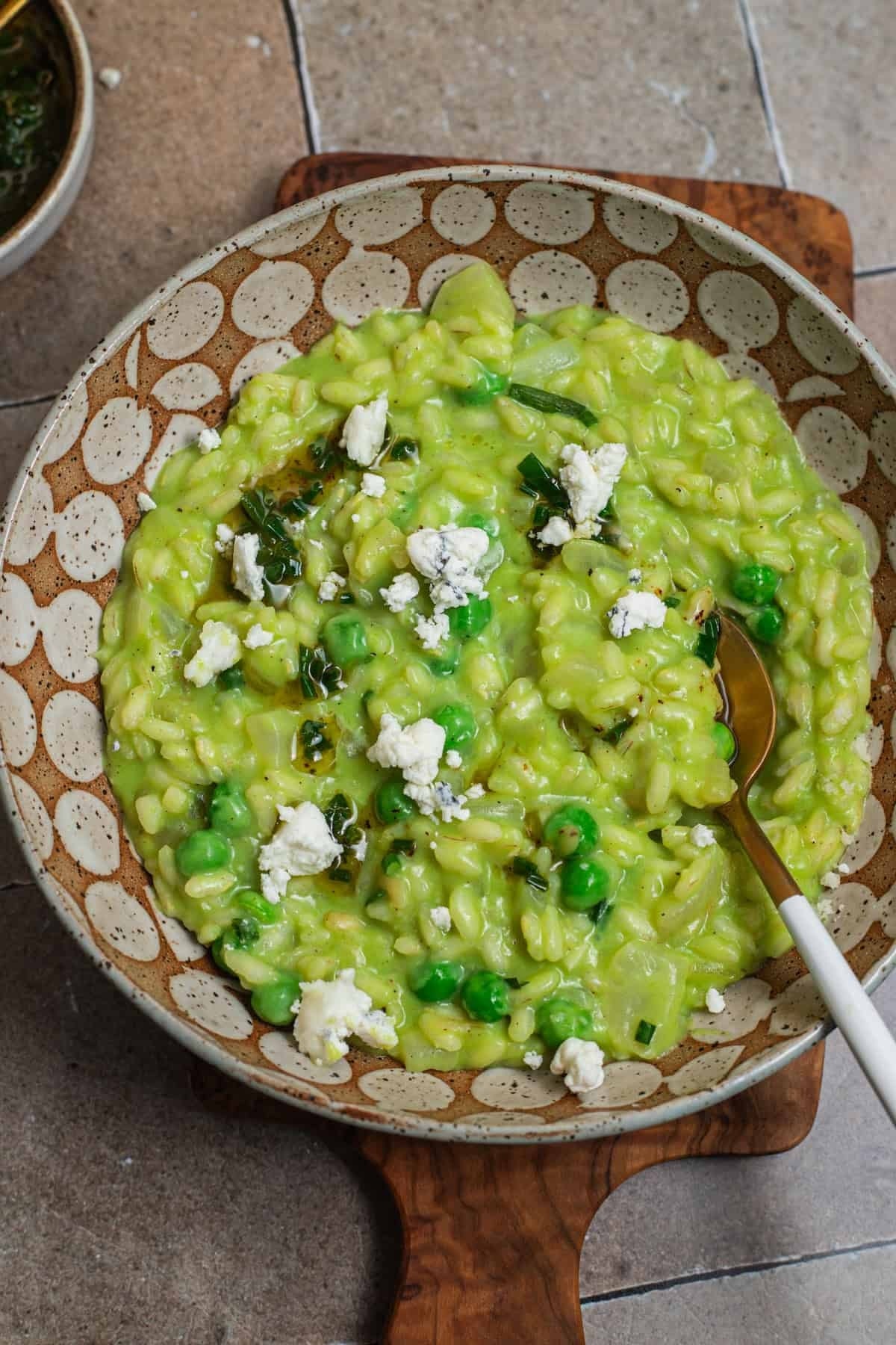 Creamy risotto with peas and crumbled cheese in a decorative bowl on a wooden board