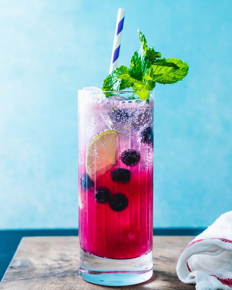 Tall glass of berry and lime sparkling drink with mint garnish and a striped straw