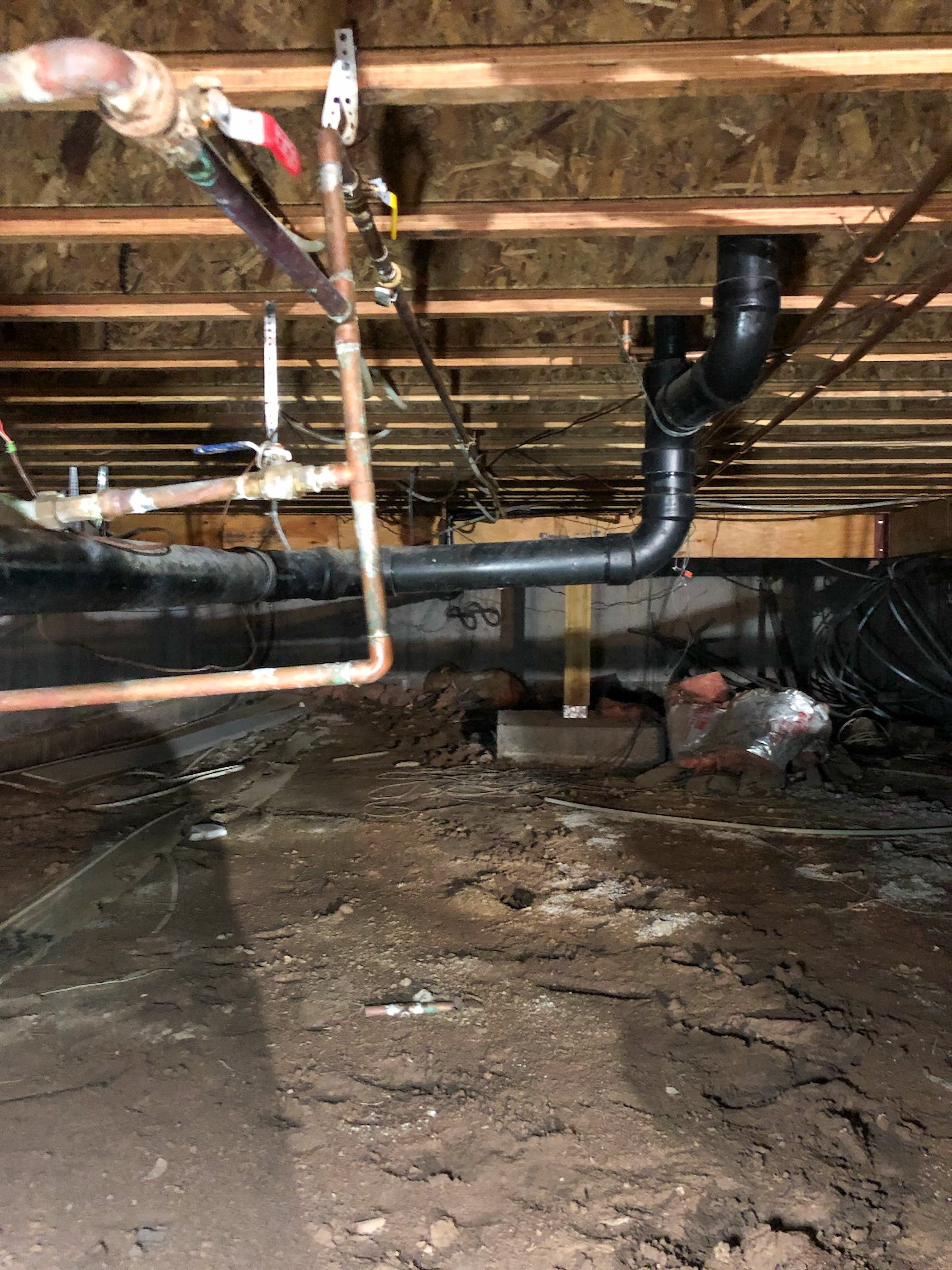 Crawl space under a house with exposed pipes and plumbing