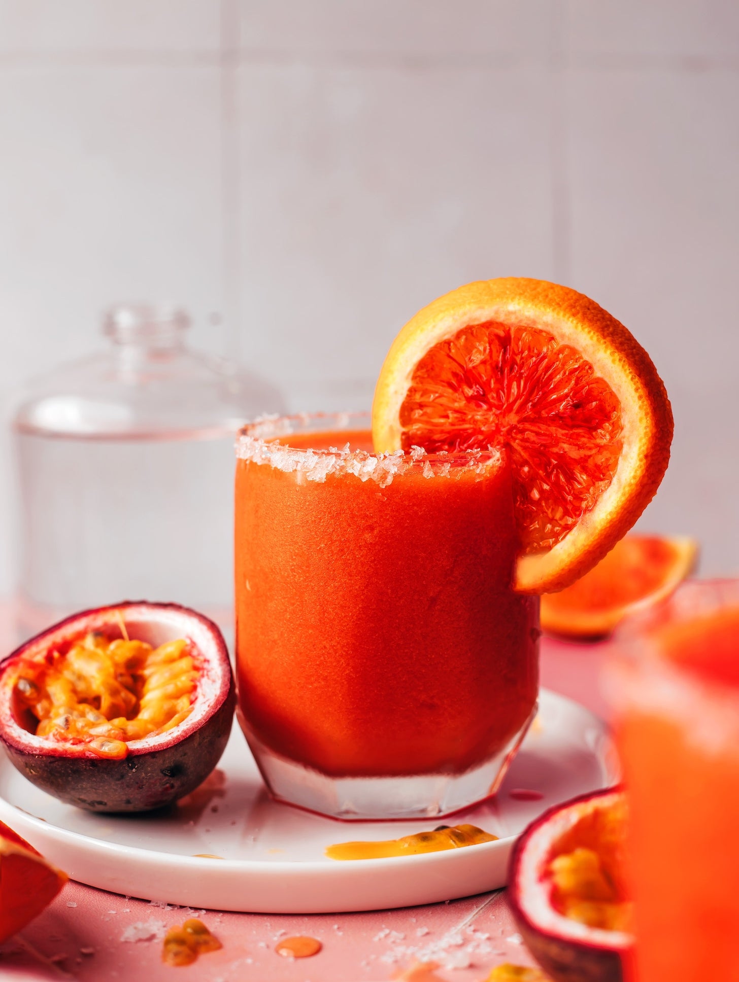 Tropical smoothie in a glass with a sugared rim, garnished with a slice of orange. Fresh passion fruit surrounds the glass on a platter