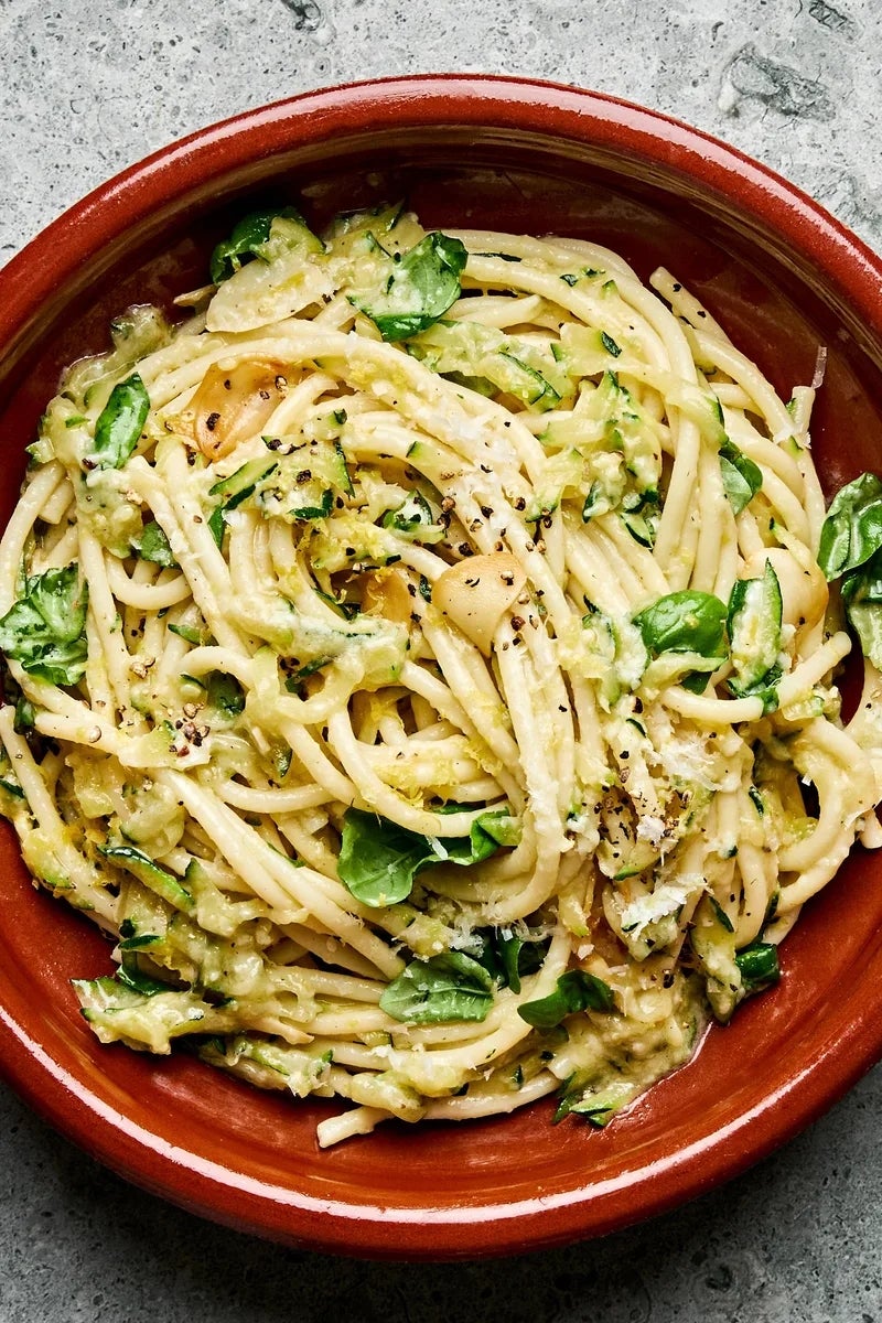 Creamy pasta with zucchini and spinach in a clay dish, topped with herbs and grated cheese