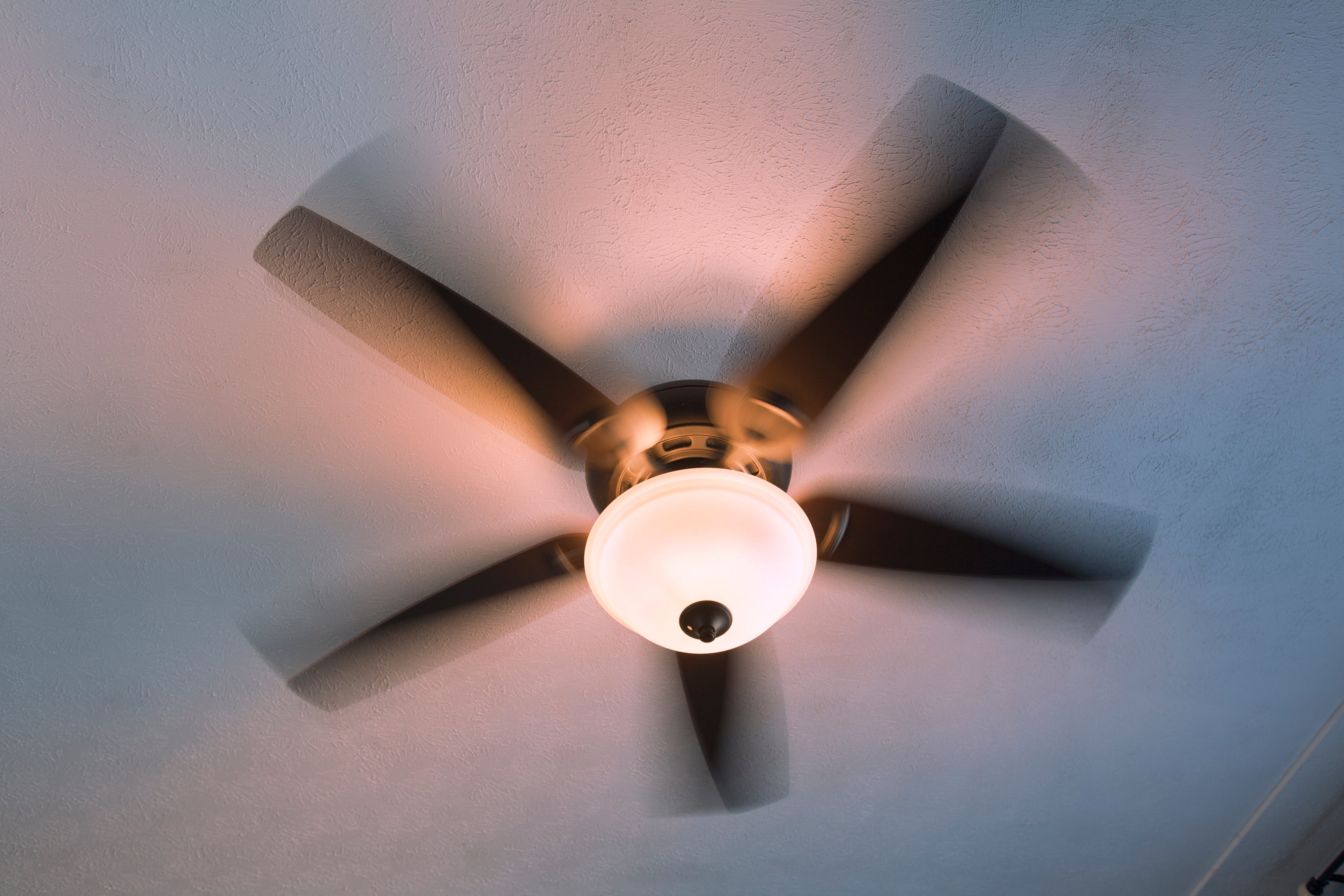 Ceiling fan spinning with four blades, attached to a light fixture, viewed from below