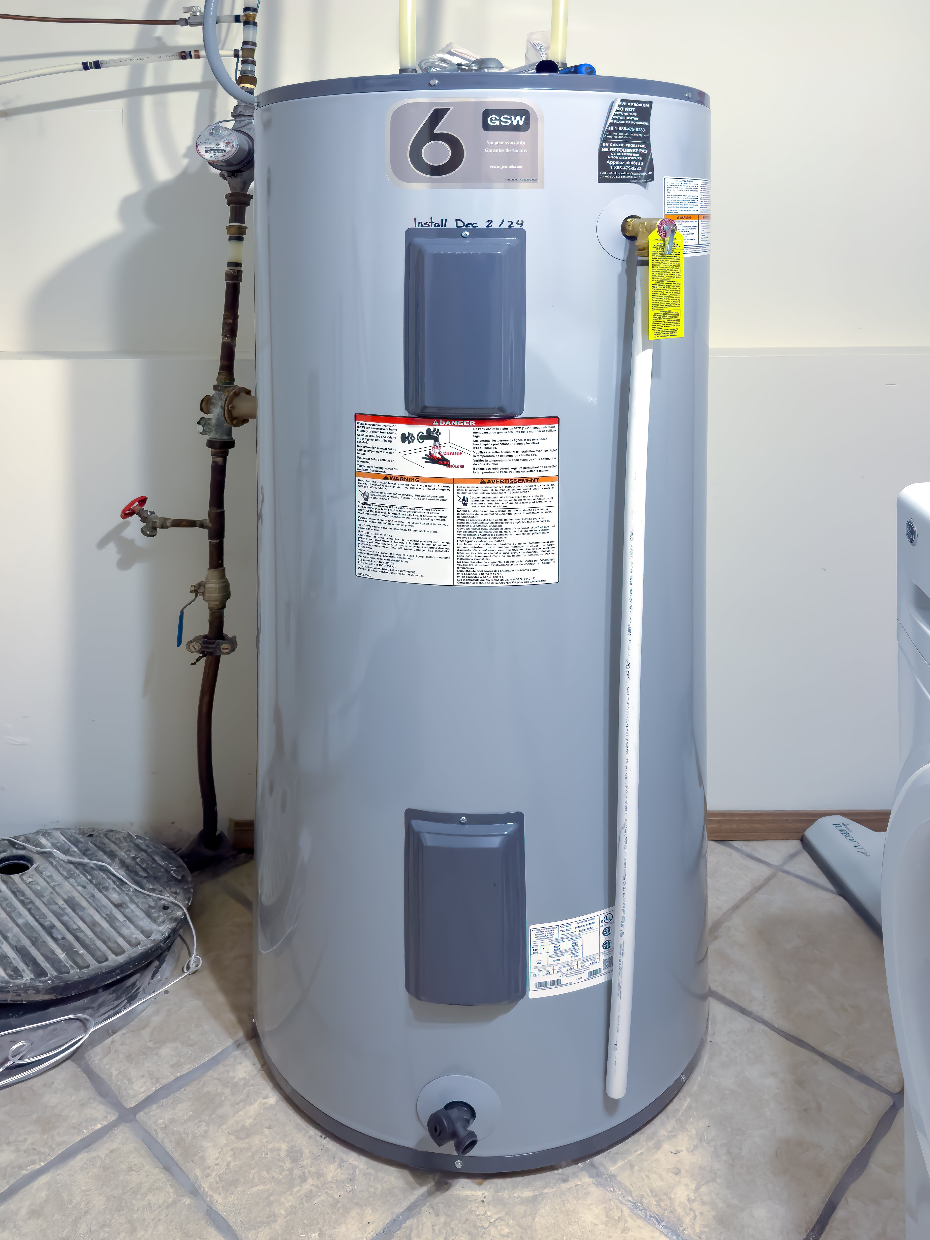 A water heater installed in a utility room, surrounded by plumbing pipes