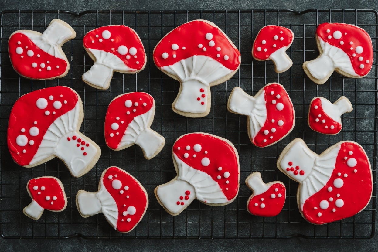 Cookies shaped like mushrooms with red and white icing, arranged on a cooling rack