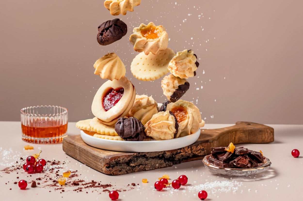Assorted cookies and pastries artfully falling onto a wooden board with a dish of chocolate pieces and red berries nearby