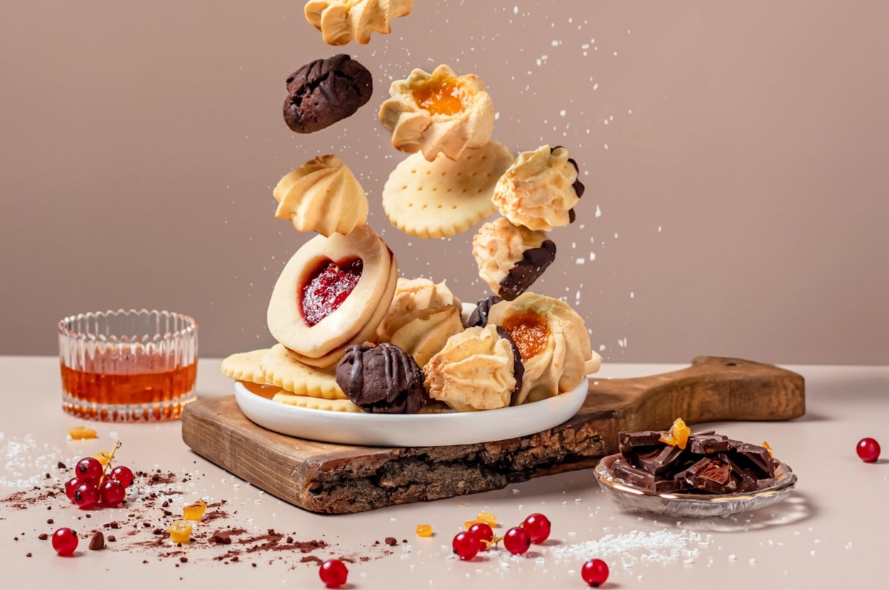 Assorted cookies and pastries artfully falling onto a wooden board with a dish of chocolate pieces and red berries nearby