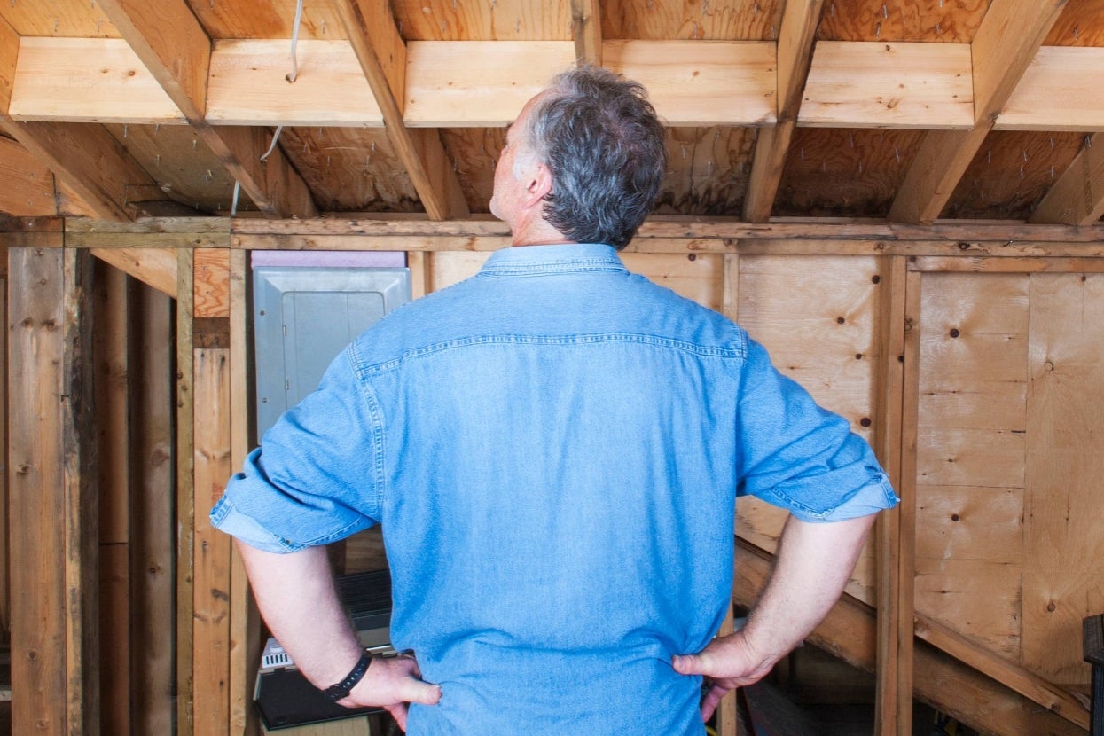 Person in a denim shirt inspects unfinished wooden beams and walls in a building under construction