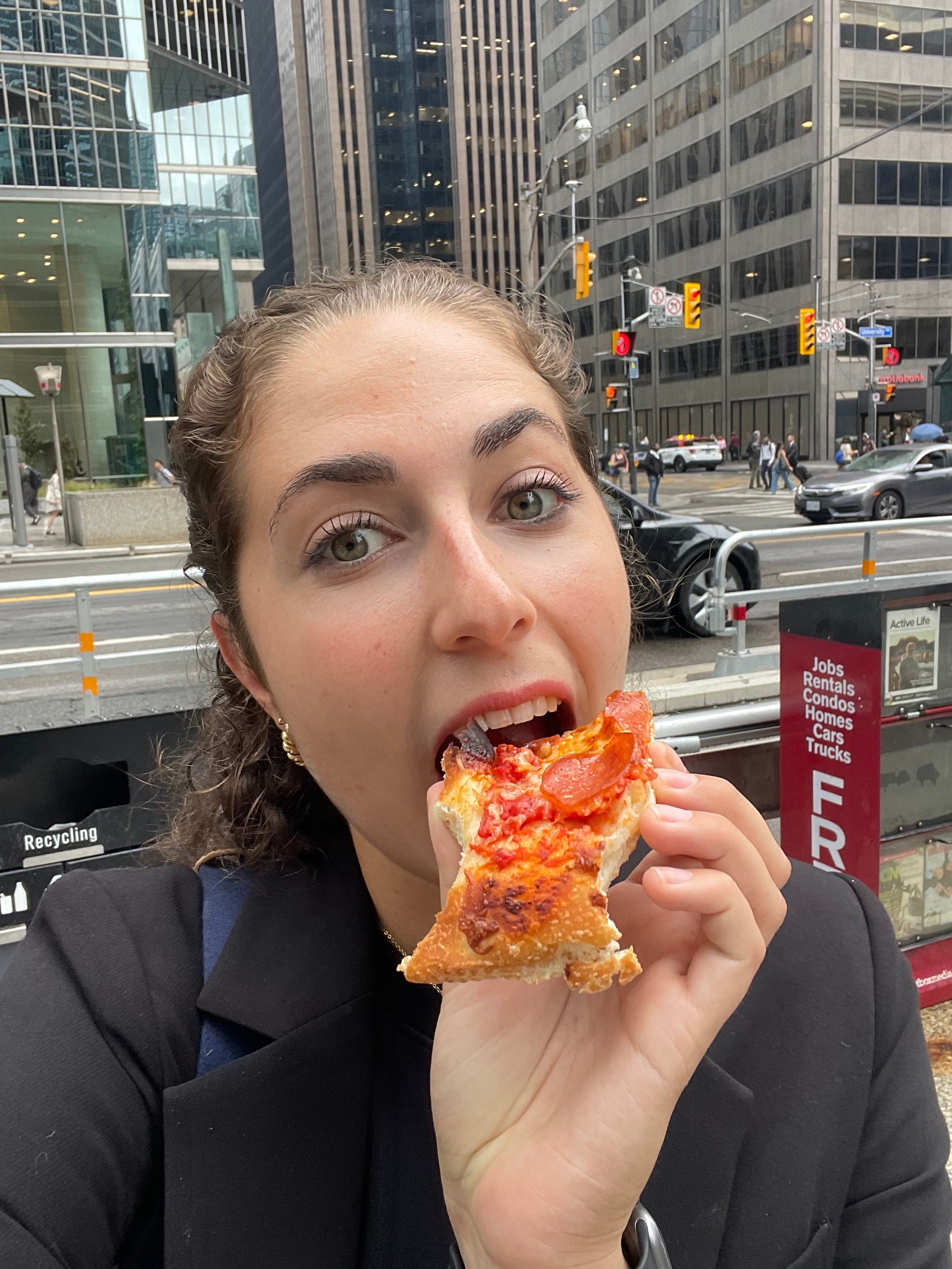 Person som spiser pizza i en bygate med skyskrapere og trafikk i bakgrunnen