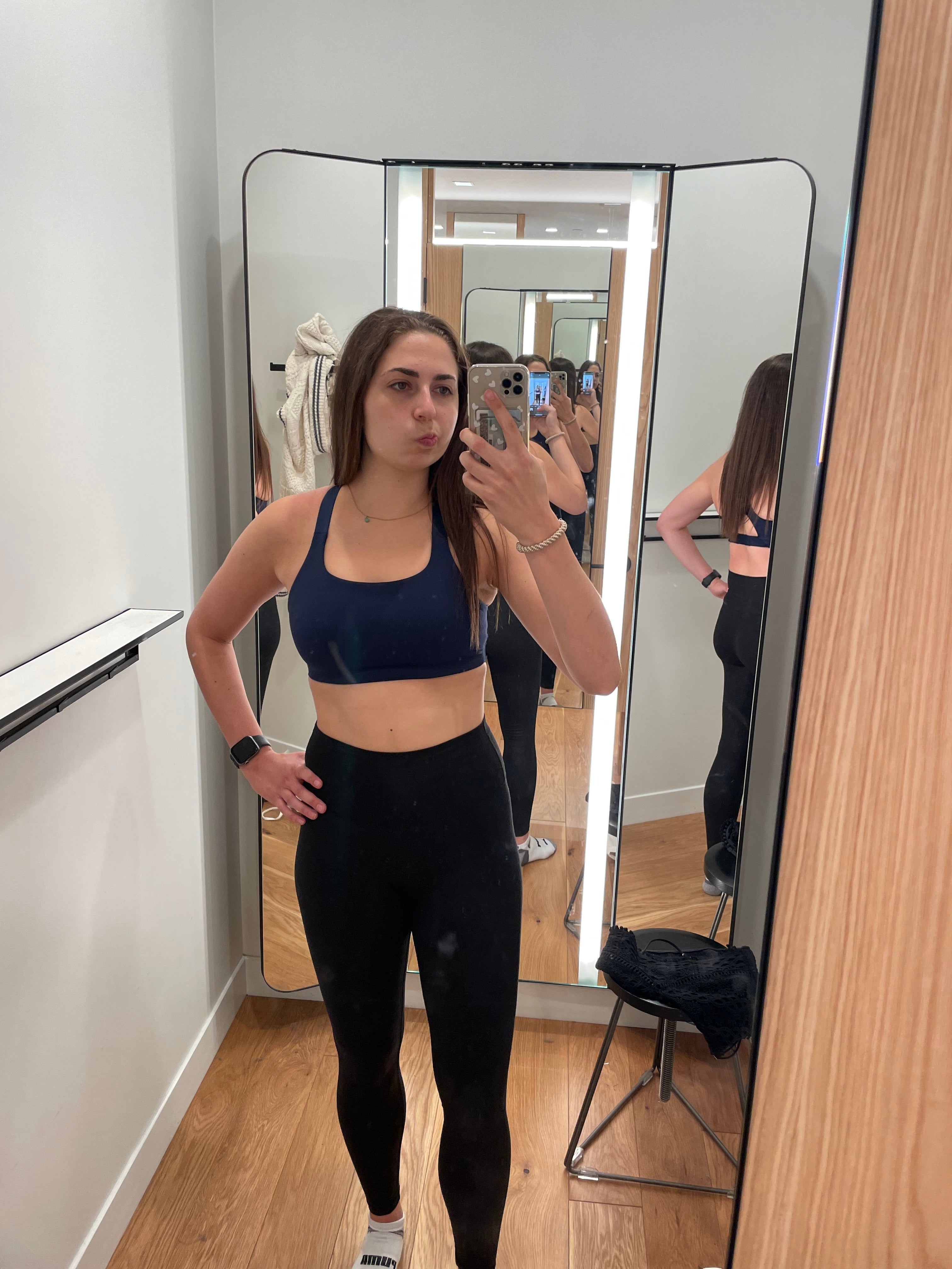 Person som tar en speilselfie i treningsantrekk, iført en sports-bh og leggings, står i et prøverom med flere speilreflekser