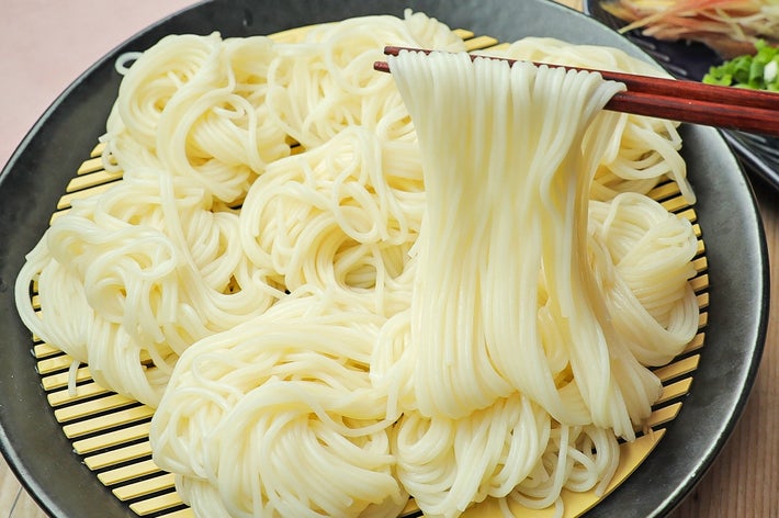 ザルに盛られた素麺を箸で持ち上げる様子。