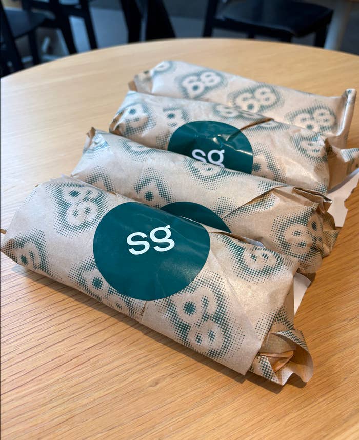 Wrapped sandwiches on a table, each with a teal sticker labeled "sg."