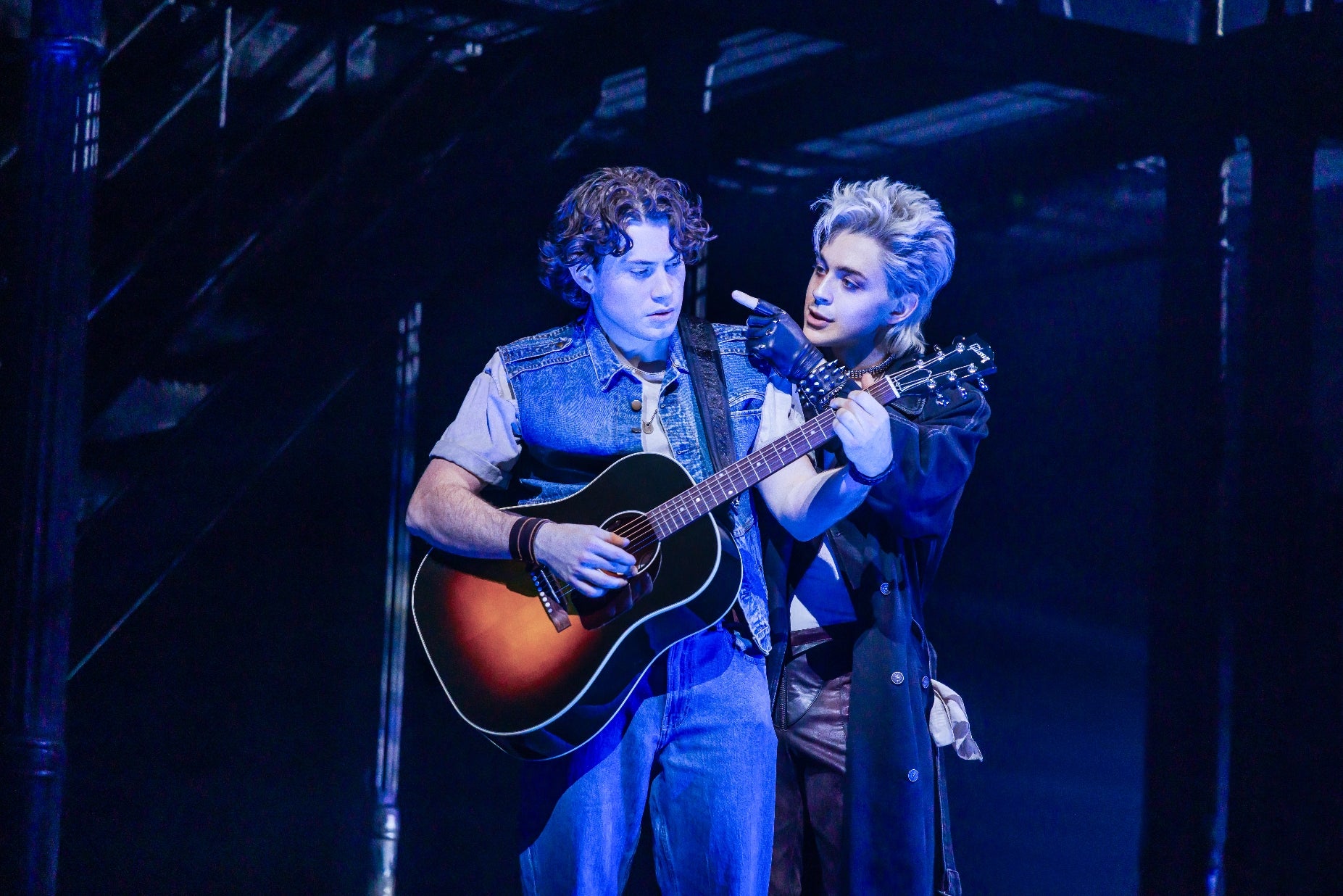 Two performers connected stage; 1 plays guitar portion the other, successful theatrical attire, gestures dramatically. The country conveys an aggravated philharmonic moment
