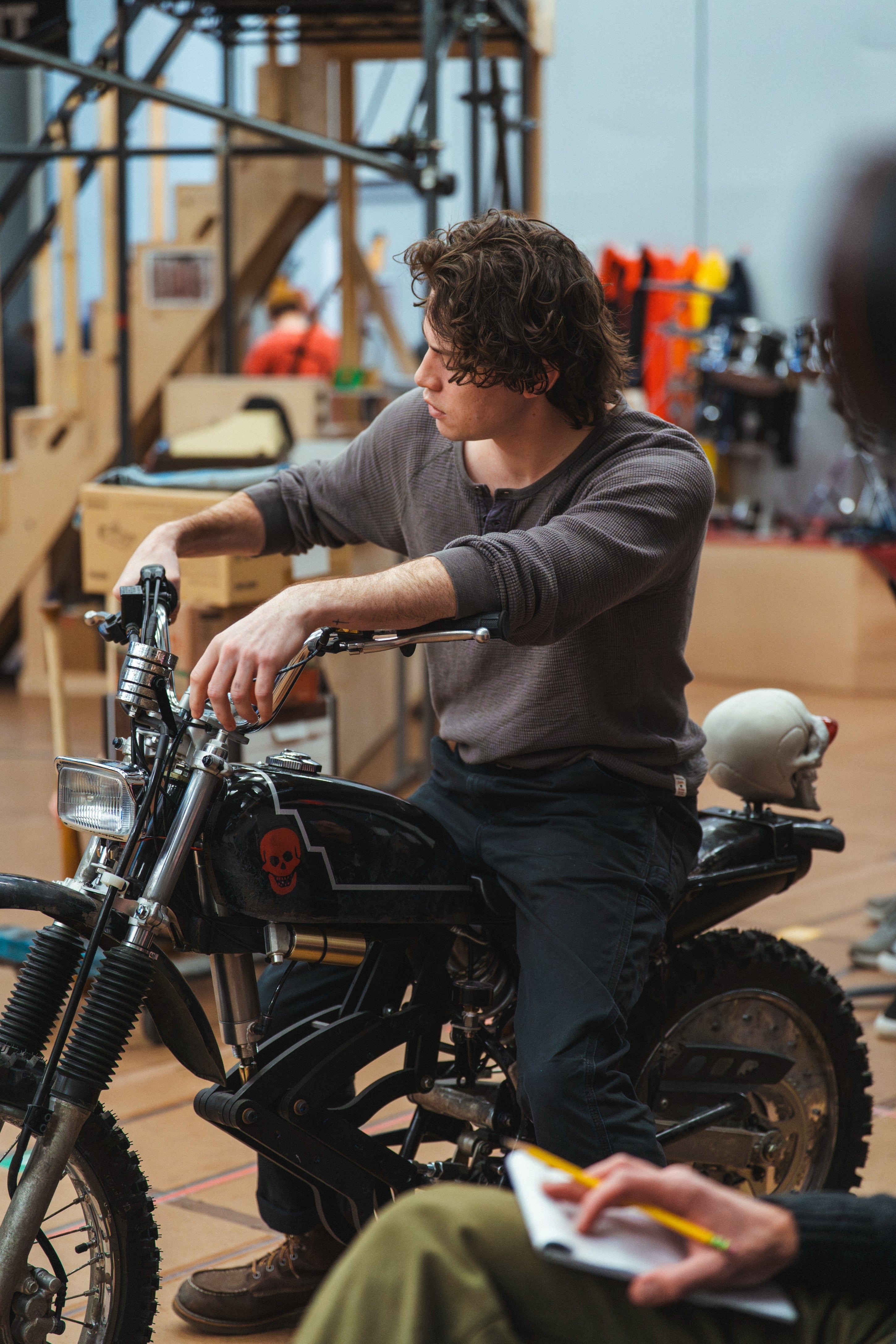 Person sitting connected a motorcycle successful a workplace setting, wearing casual attire, looking to the side