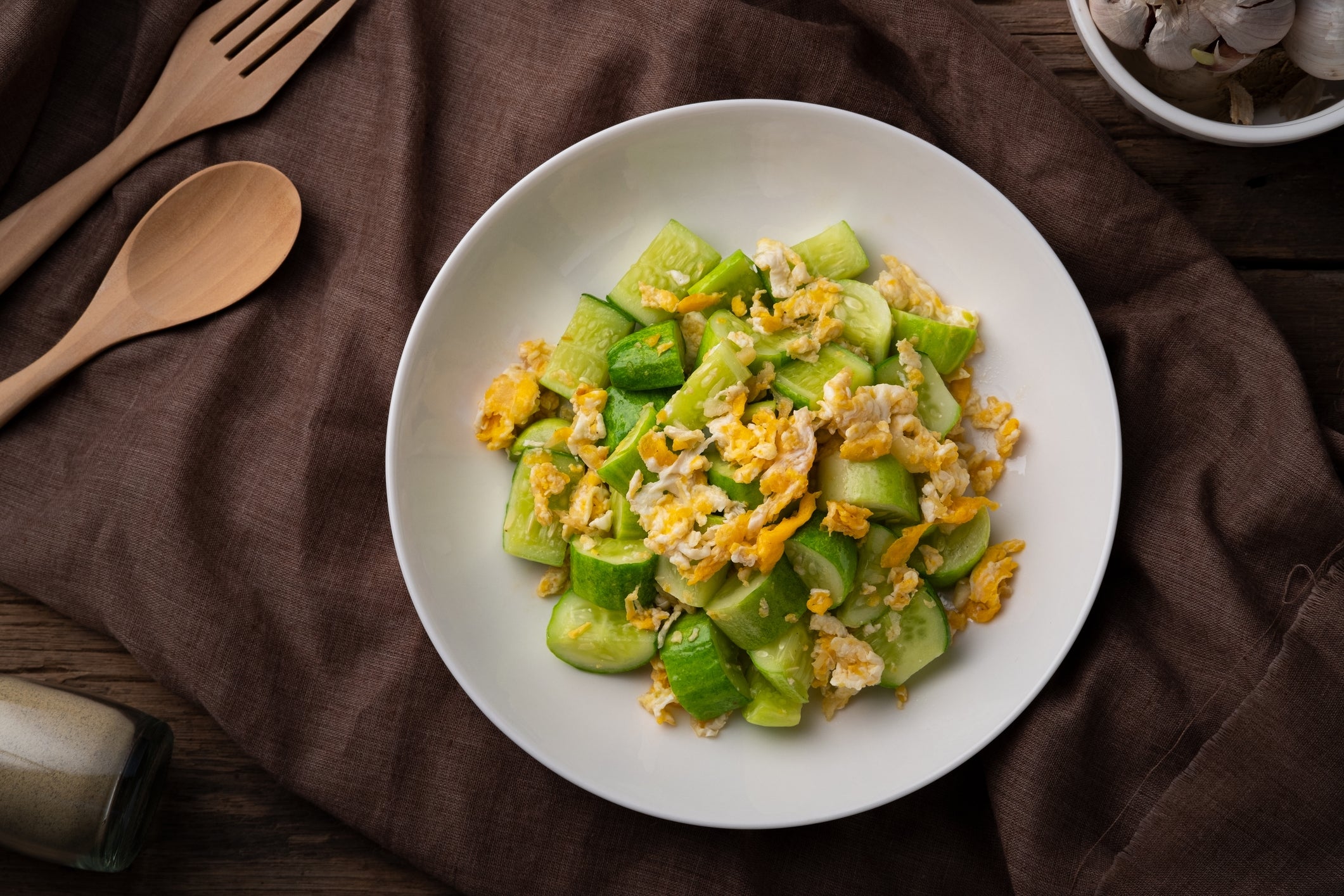 A sheet of diced cucumbers and scrambled eggs connected a array with woody utensils nearby