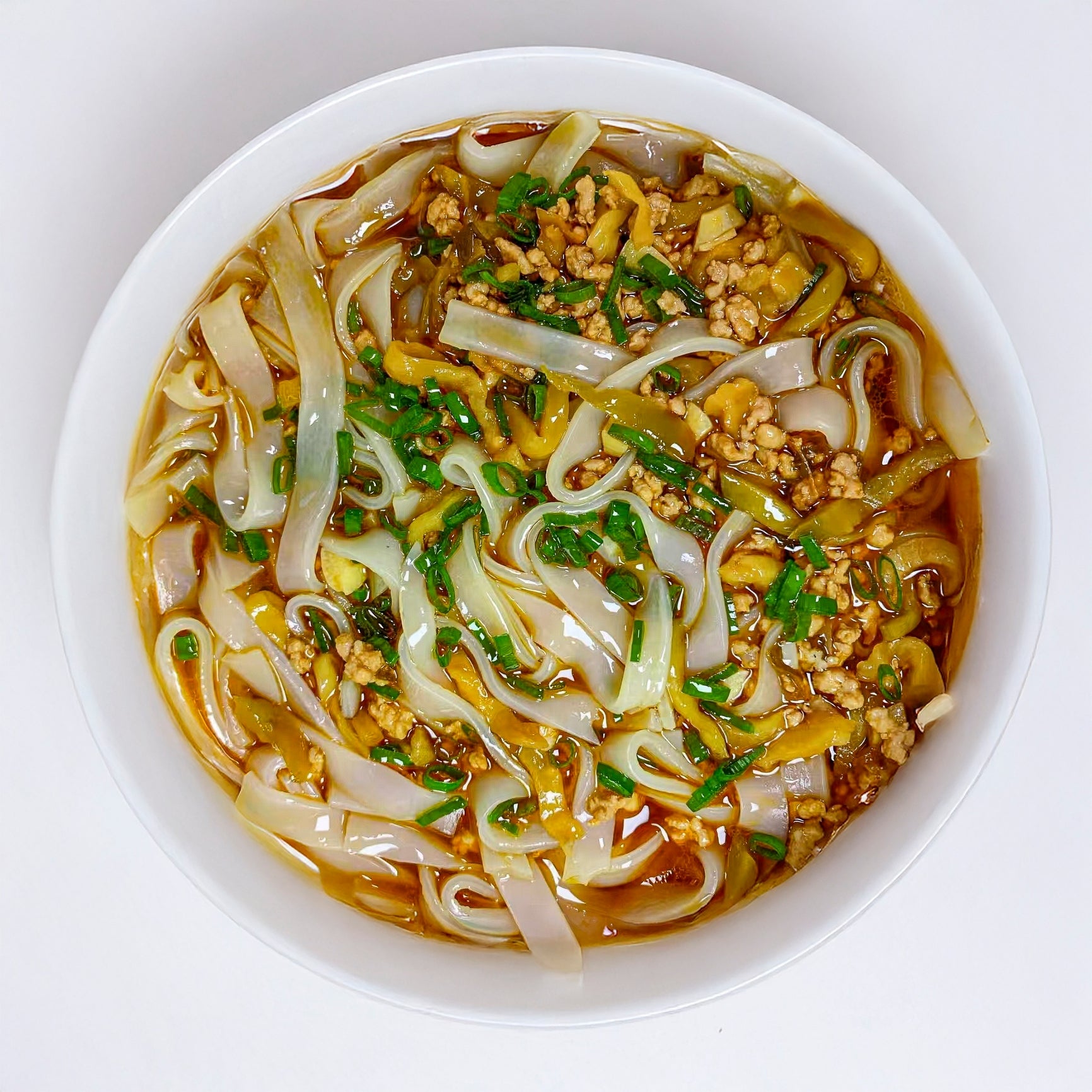 A vessel of noodle crockery with sliced vegetables and minced meat, garnished with herbs