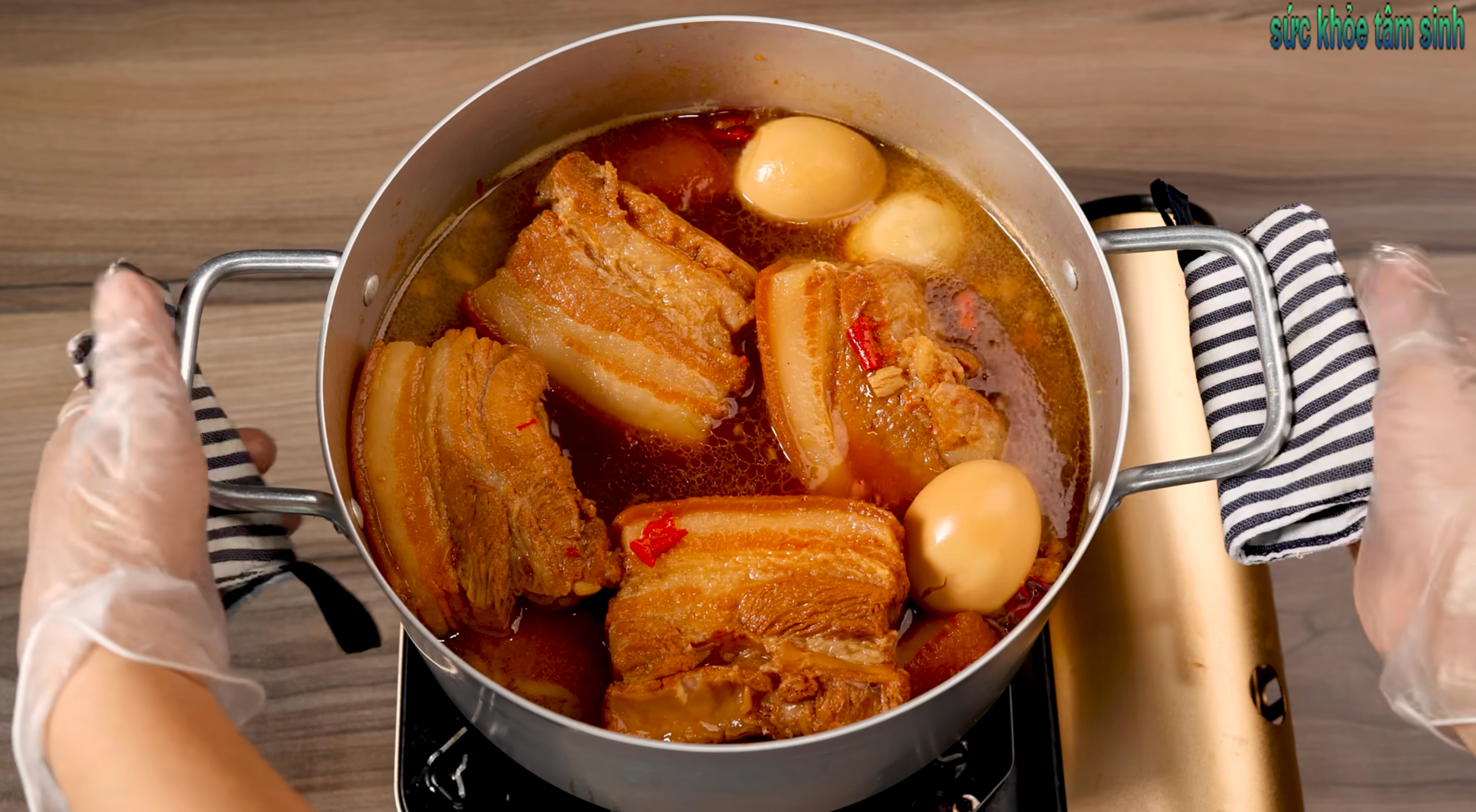Hands holding a cookware of braised pork belly with eggs simmering successful broth