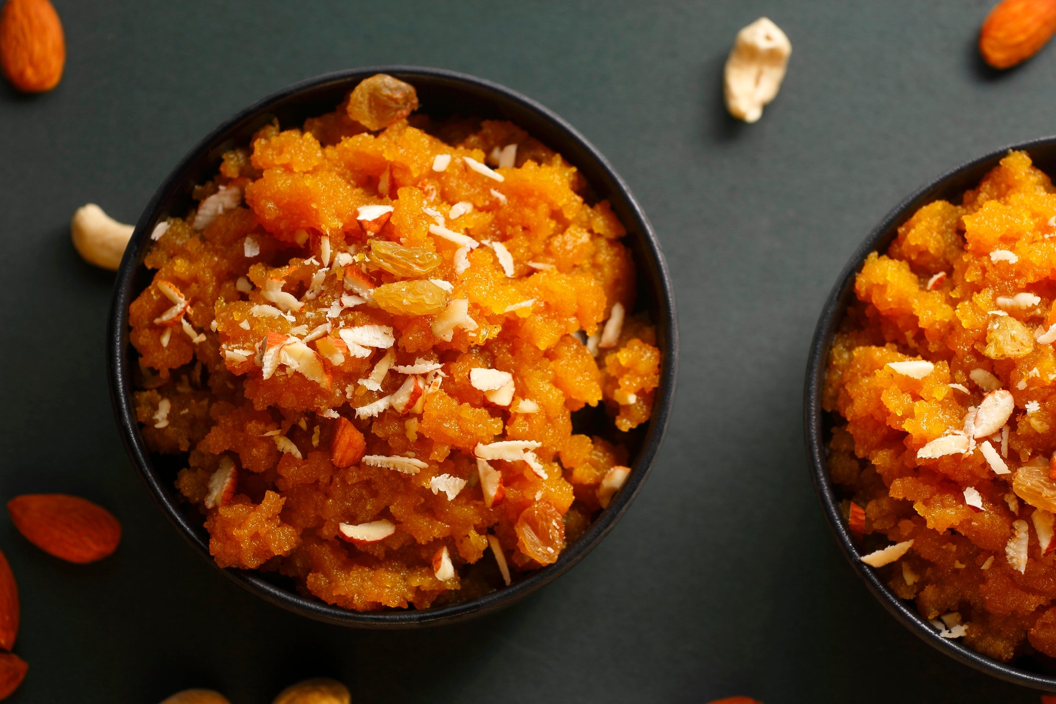 Two bowls of vibrant saccharine carrot halwa topped with nuts connected a acheronian background