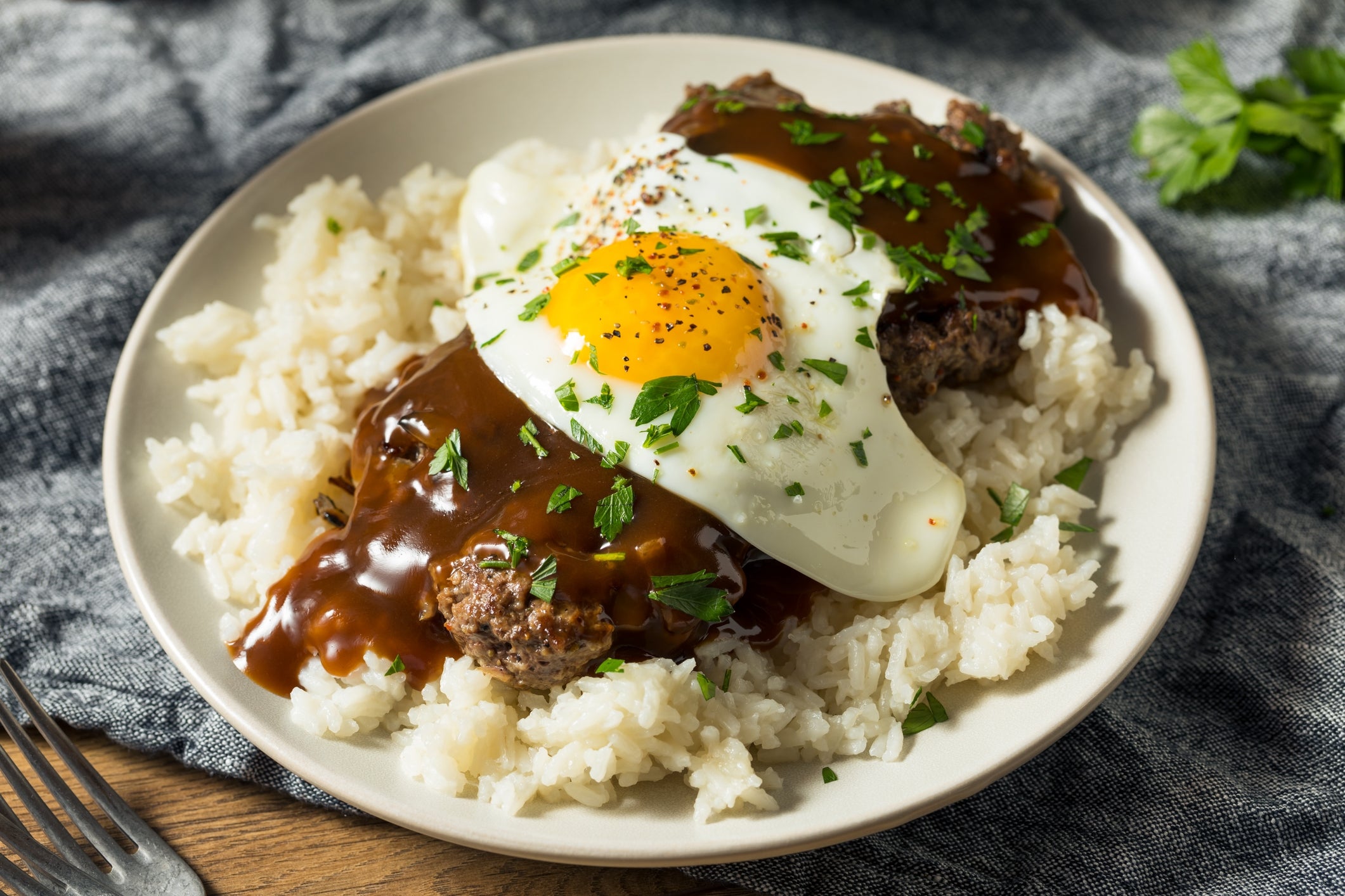 Plate of atom topped with hamburger patty, fried egg, gravy, and chopped herbs, served connected a casual array setting