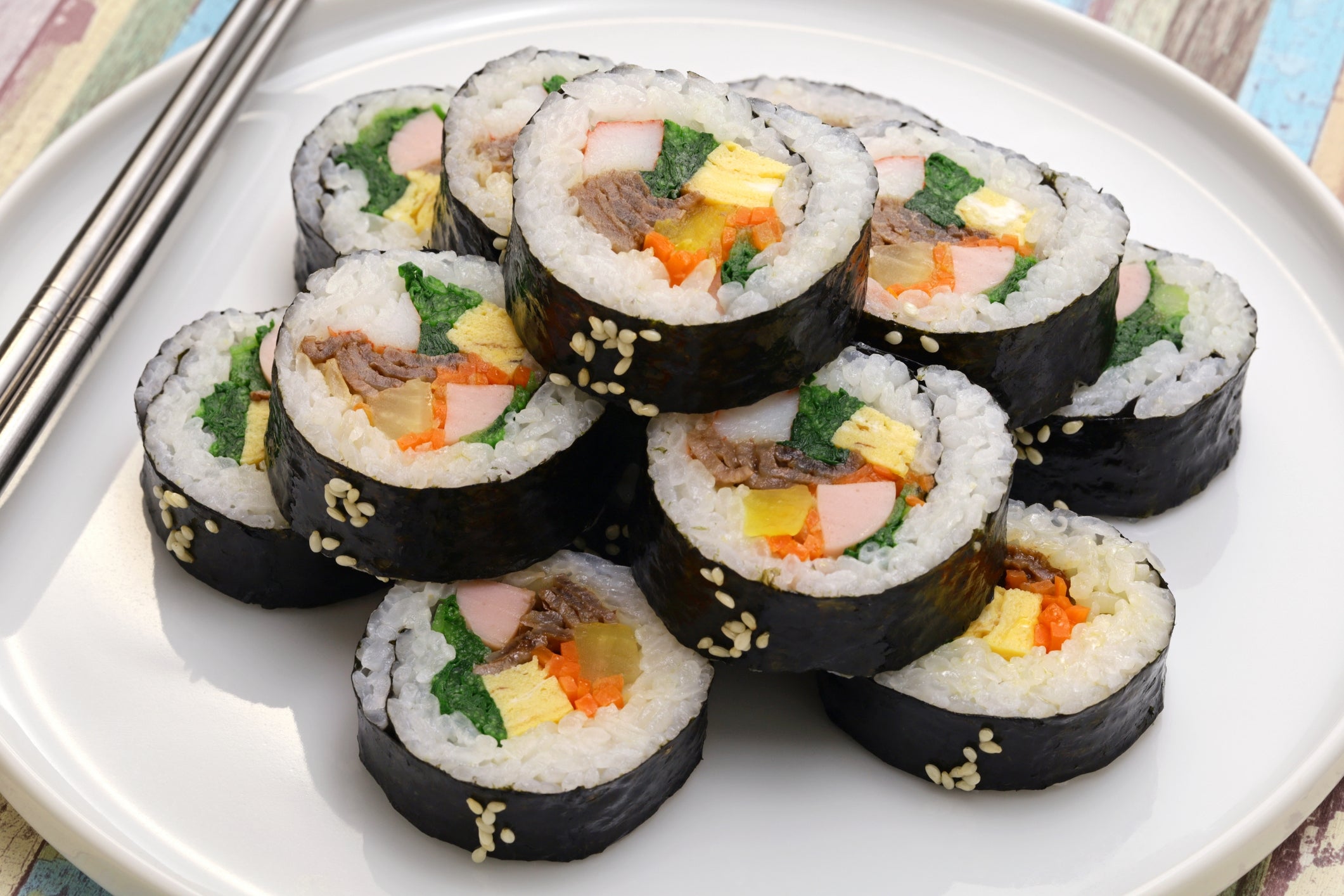 Plate of neatly arranged sushi rolls with assorted fillings, including vegetables and meat, adjacent to a brace of chopsticks