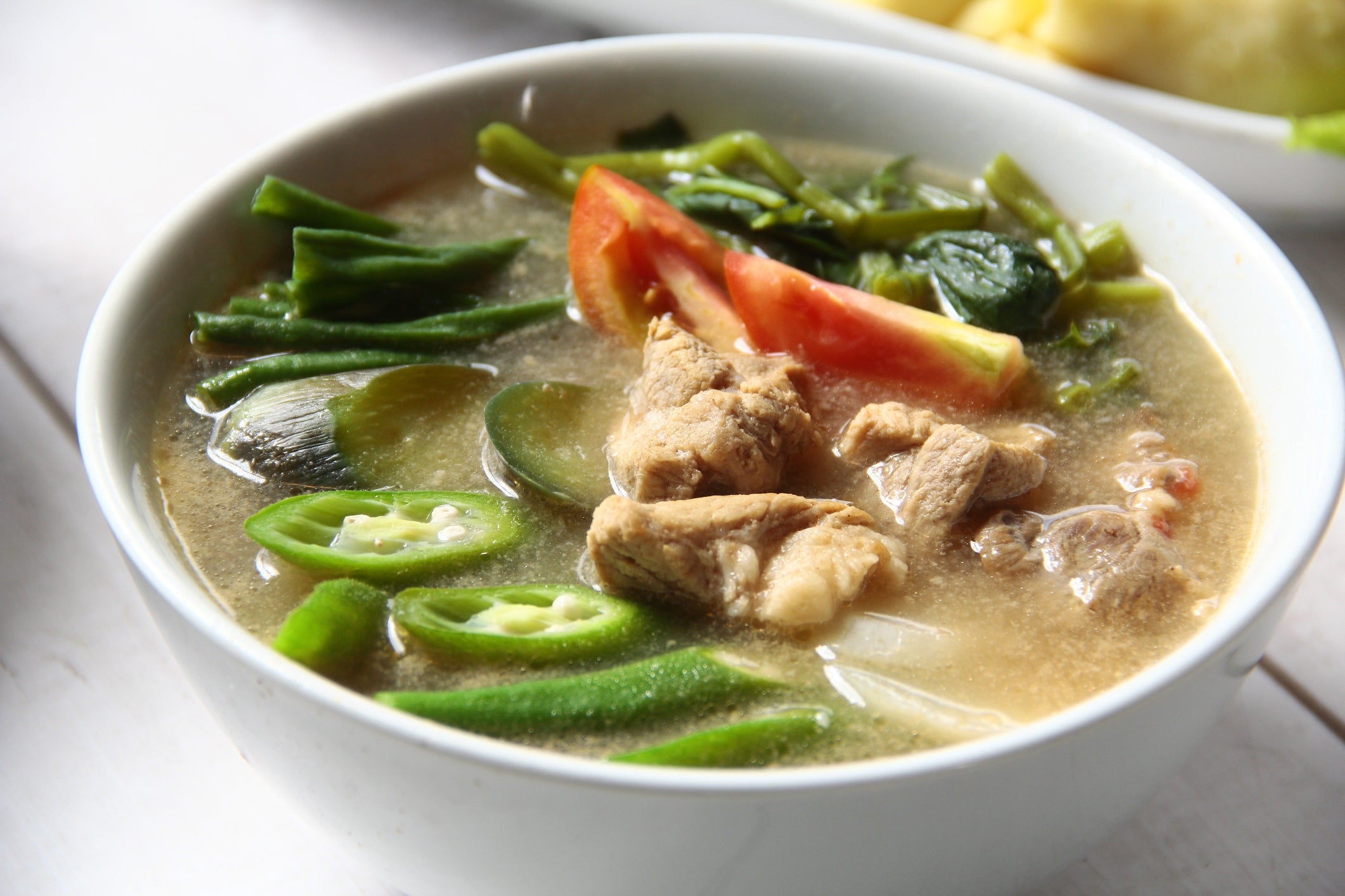 A vessel of savory crockery with chunks of meat, sliced okra, tomato, and leafy greens successful a flavorful broth