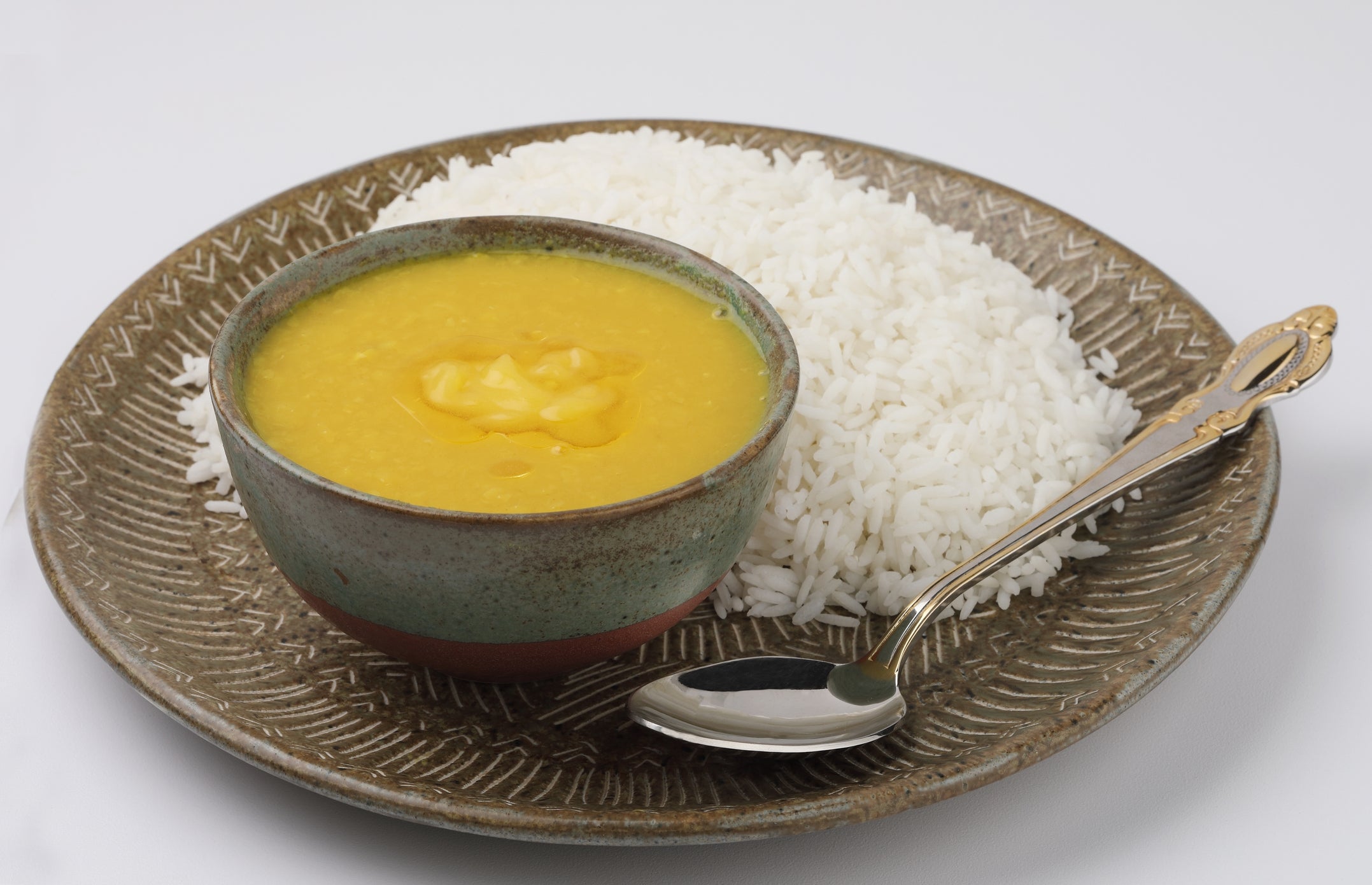 A vessel of yellowish lentil crockery with a dollop of butter, served connected a sheet with achromatic atom and a metallic spoon