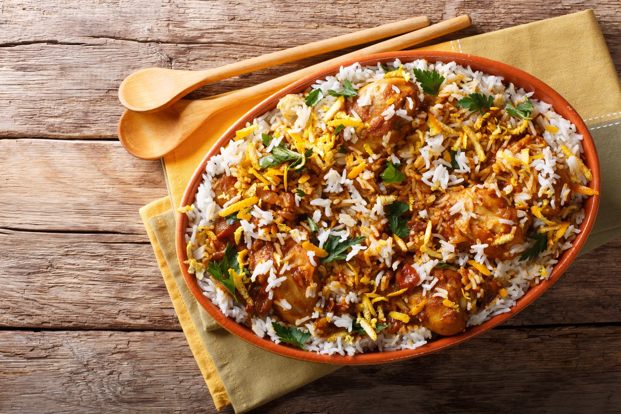 A crockery of biryani, featuring rice, marinated chicken, and garnished with herbs, served successful an oval crockery connected a woody table