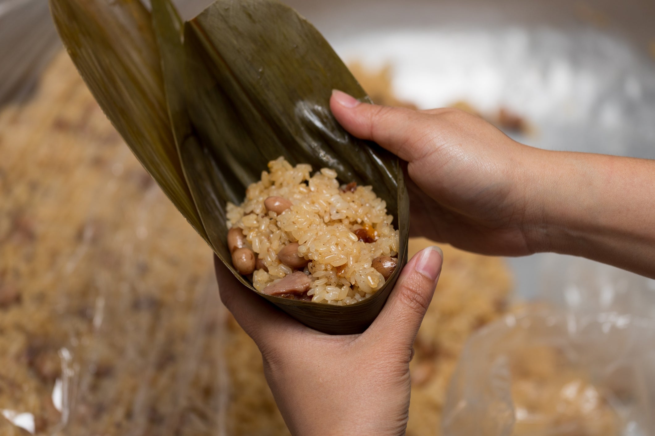 Hands wrapping sticky atom with peanuts and meats successful a banana leaf, an Asian crockery preparation