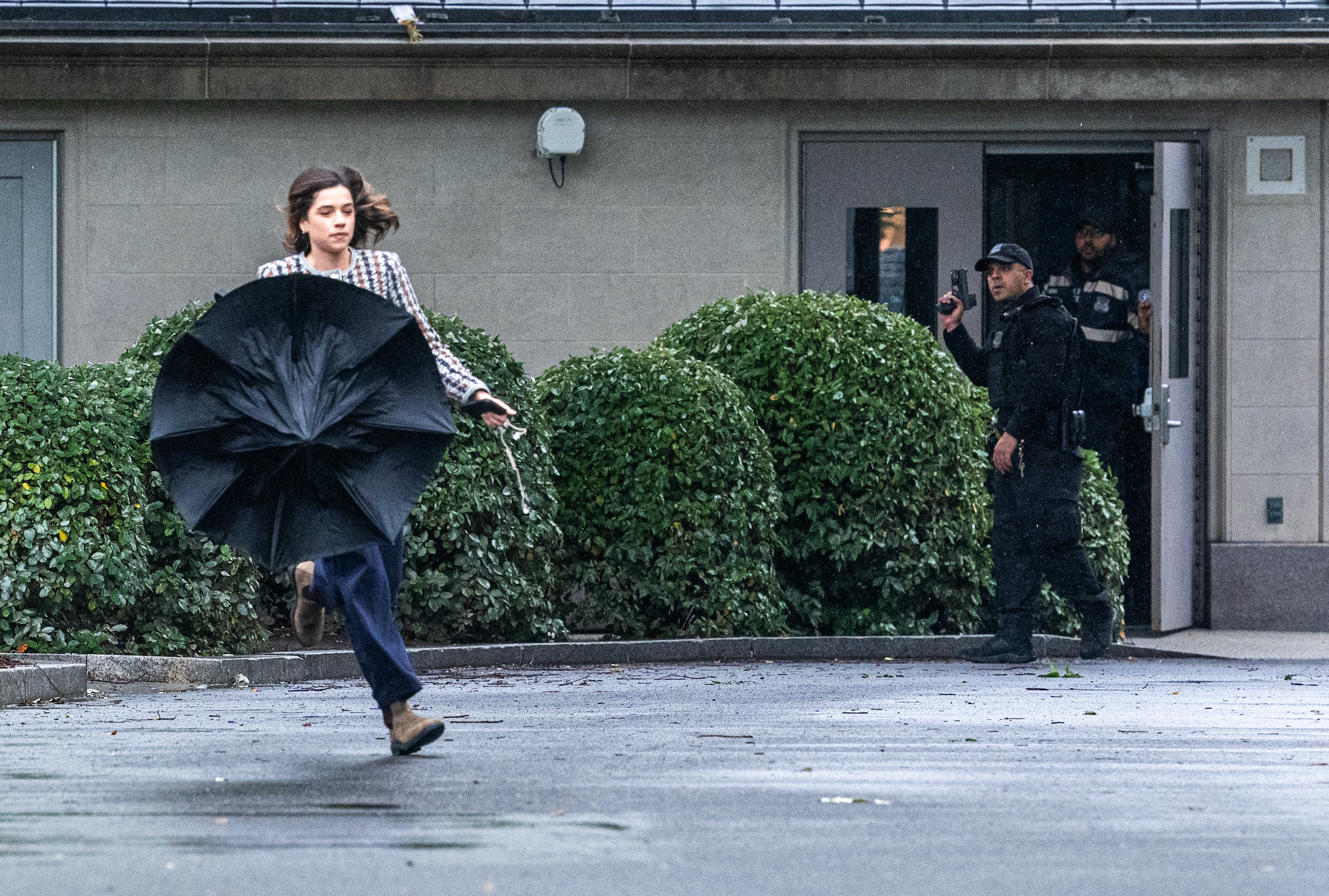 Person running with closed umbrella; security officer in background near building entrance