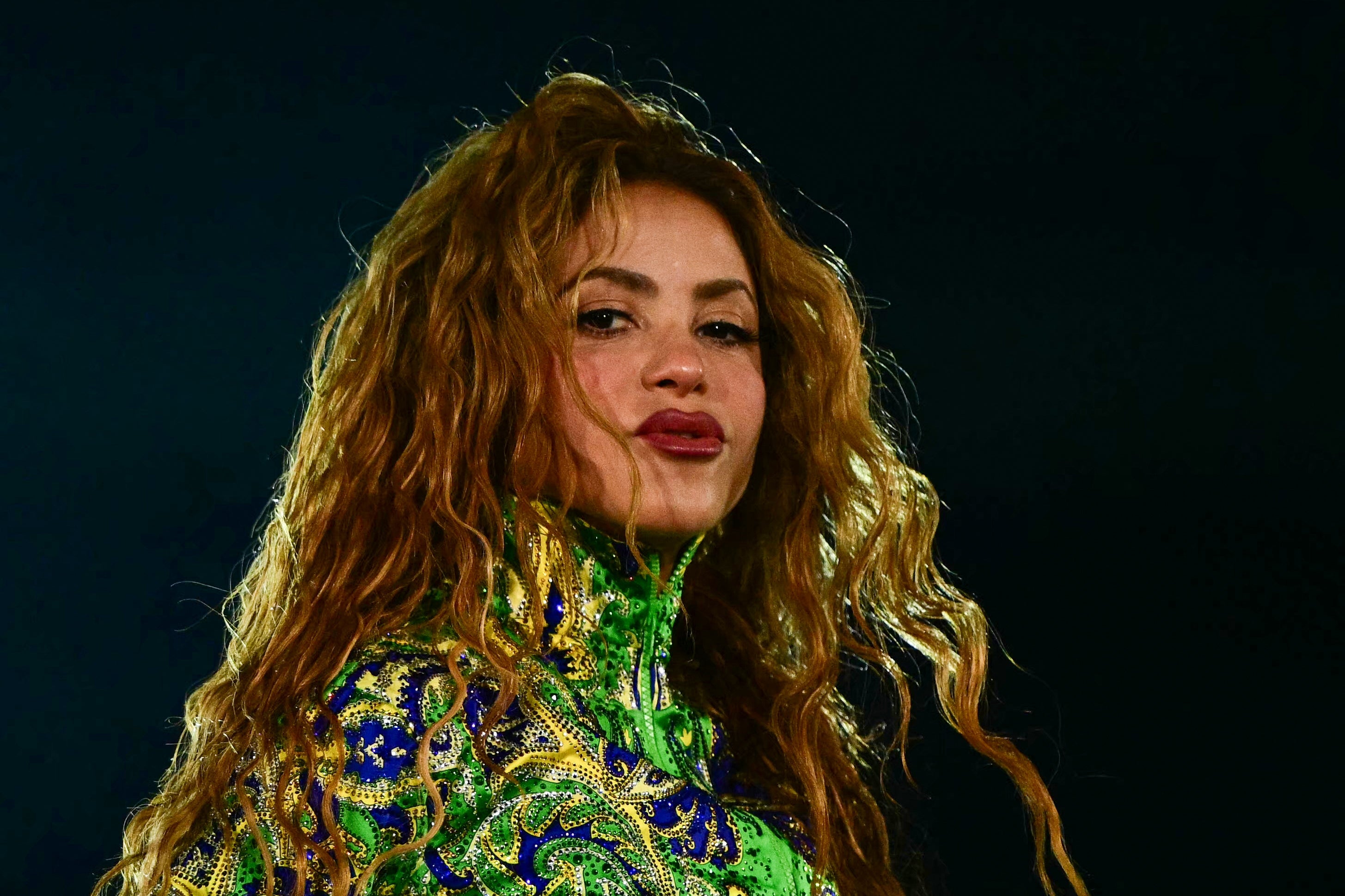 Person with long, wavy hair wearing an intricate patterned high-neck outfit, posing confidently