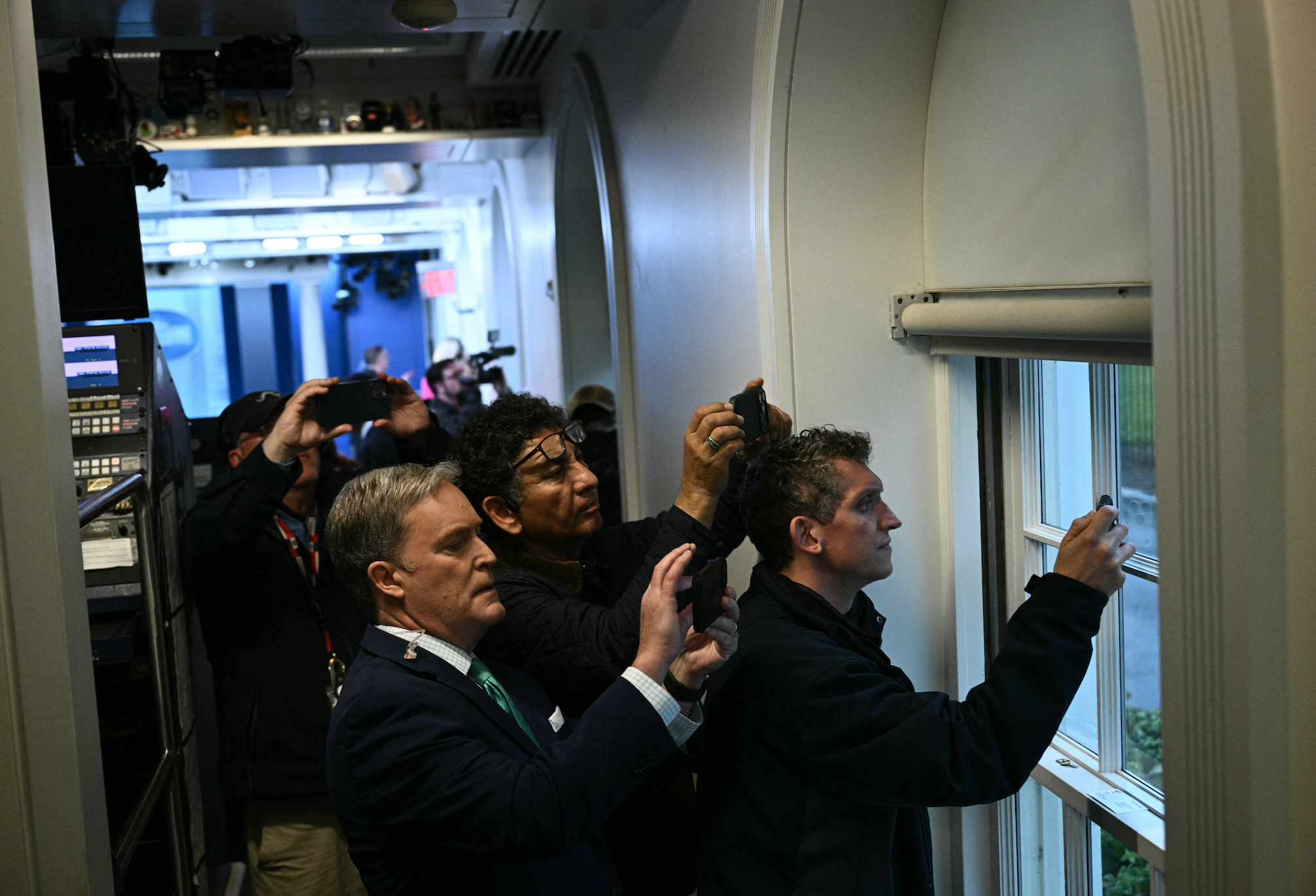 Reporters taking photos through a window in a press area, capturing an event outside