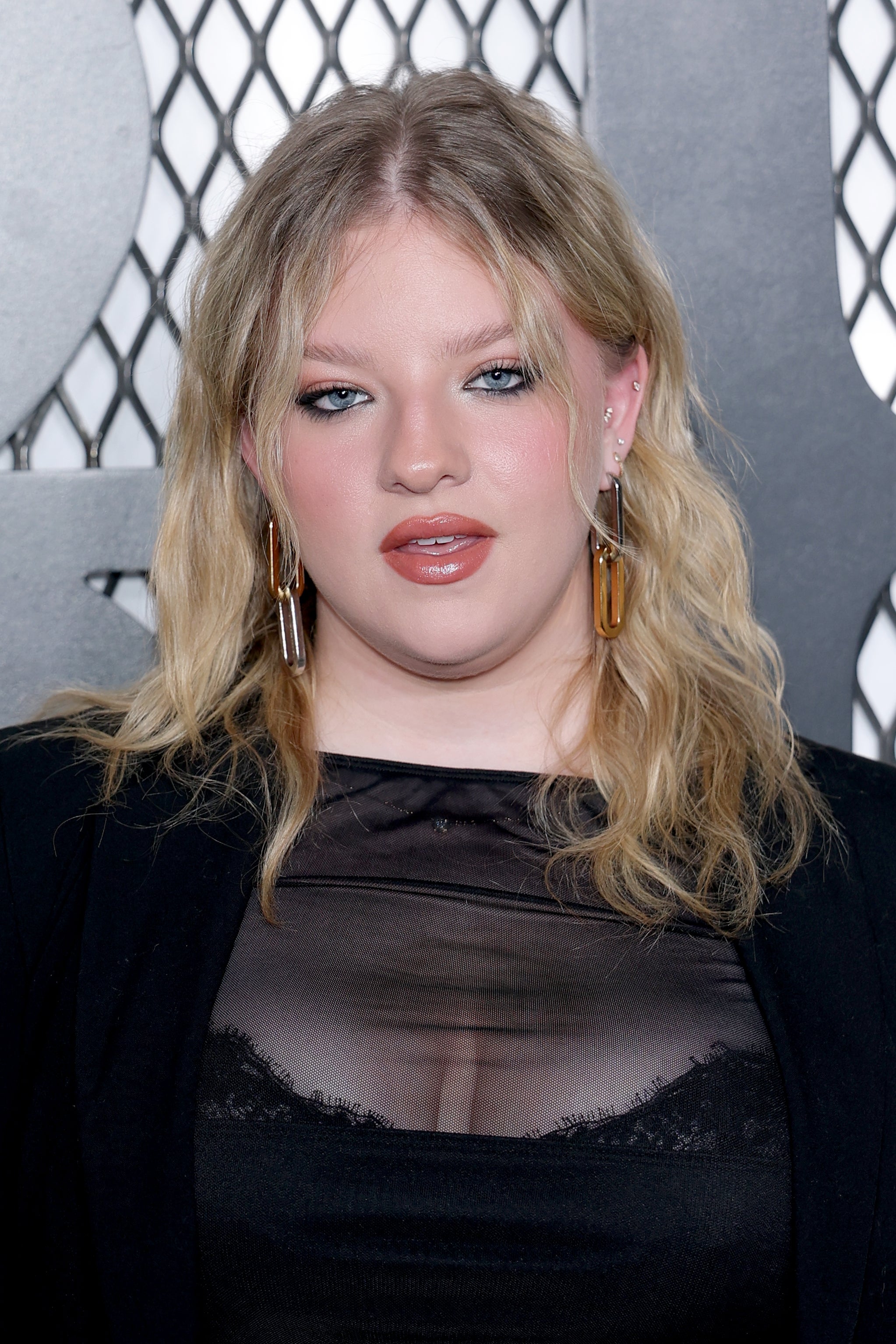 Francesca Scorsese wearing a sheer apical  and blazer stands successful  beforehand   of a patterned backdrop