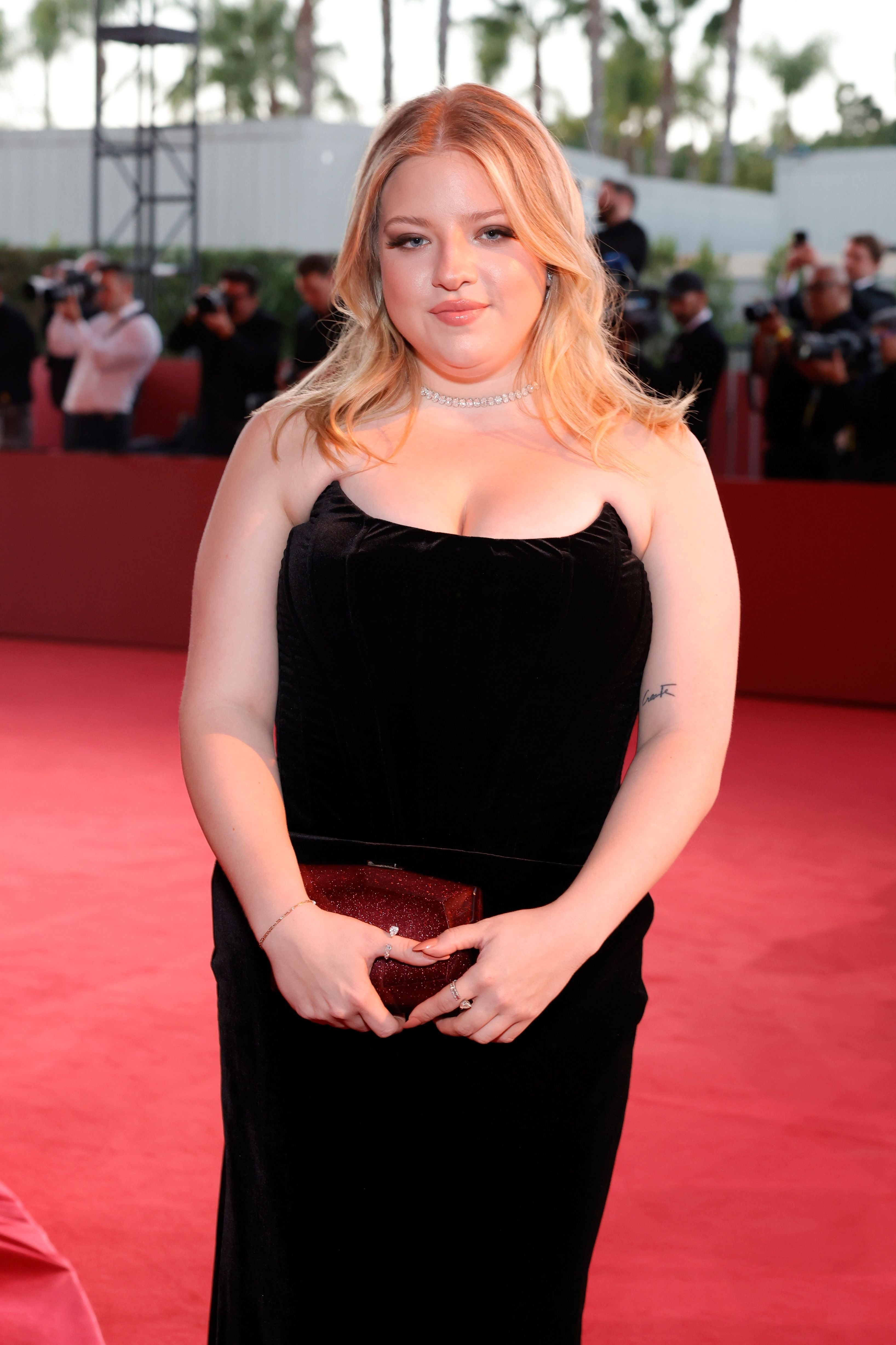 Francesca Scorsese successful  a sleek strapless gown and choker poses connected  the reddish  carpet, holding a clutch, with photographers successful  the background