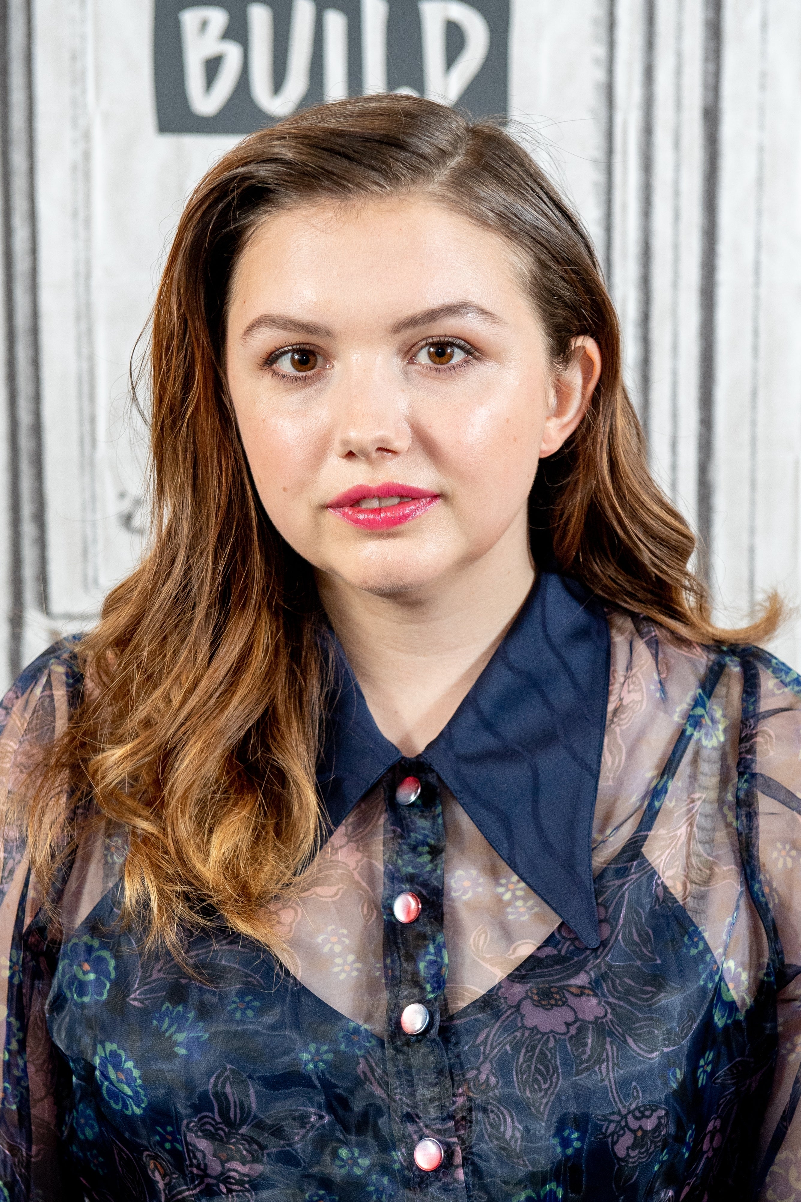 Person with long hair in a sheer floral blouse at an event