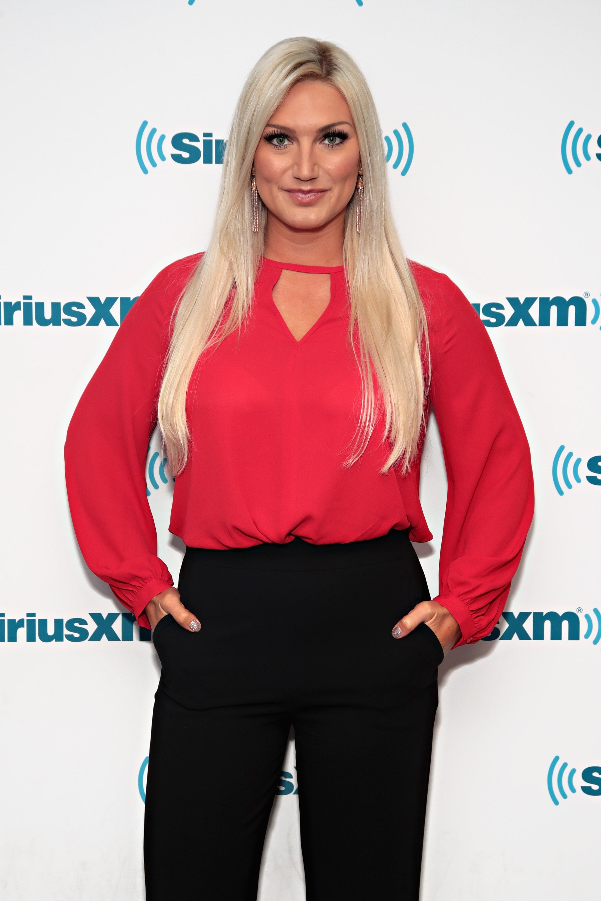 Brooke Hogan in stylish blouse and black pants poses confidently at a SiriusXM event backdrop