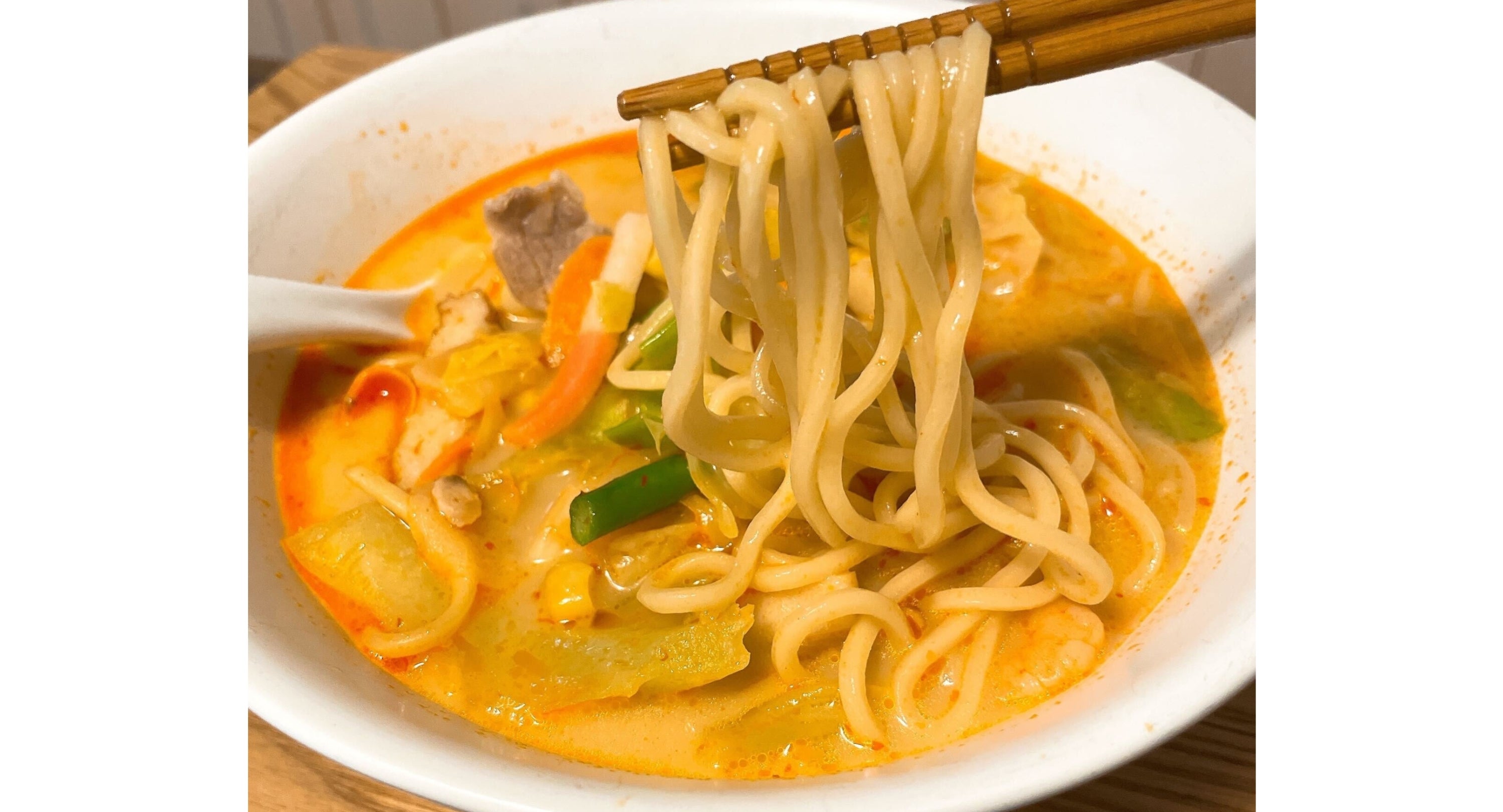 ちゃんぽんのボウルから箸で麺を持ち上げている様子。スープには野菜と具材が入っている。