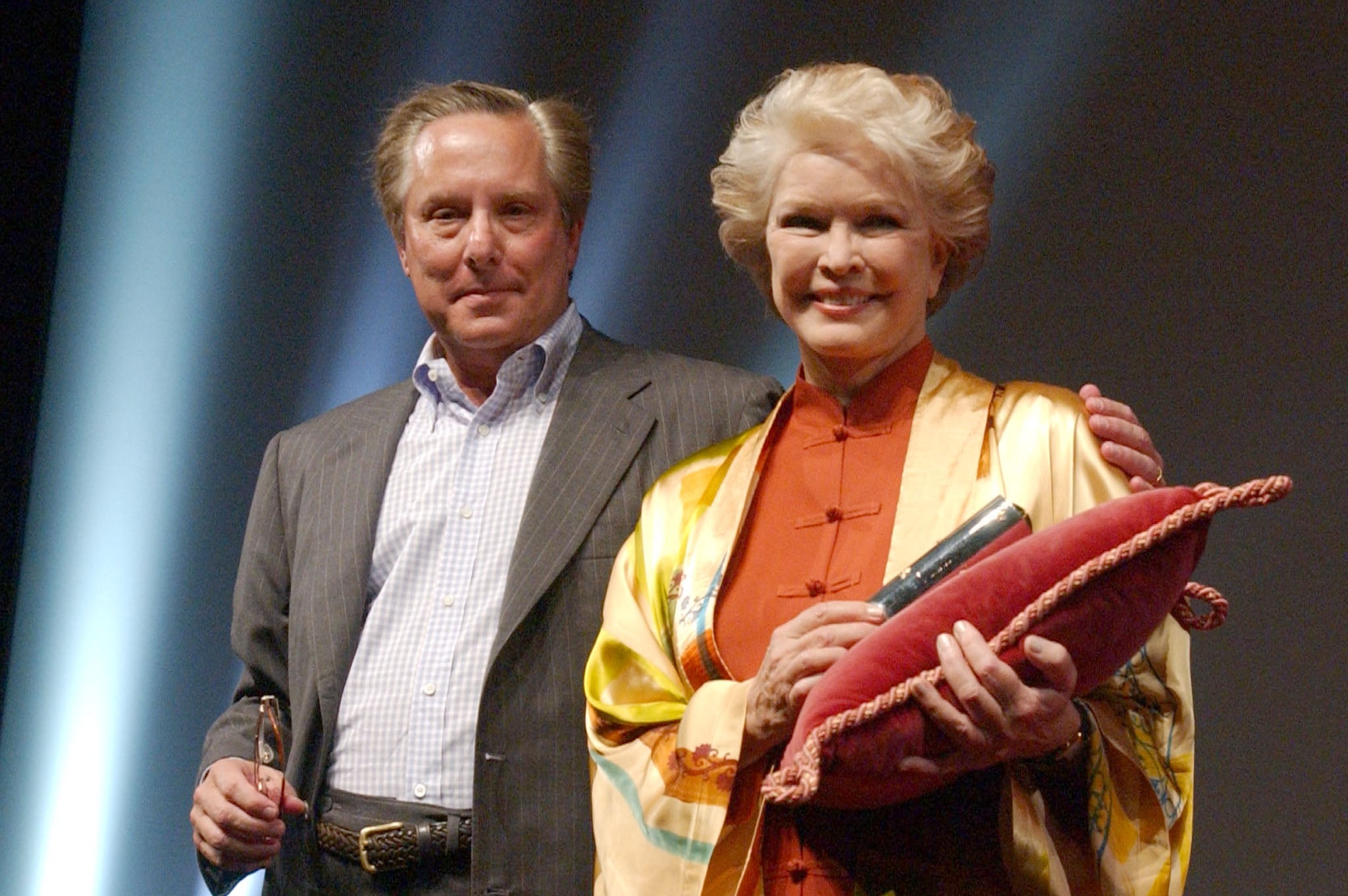 Two individuals basal   together. The idiosyncratic   connected  the close    holds a pillow with a scroll. They are wearing elegant attire with a robe-like overlay