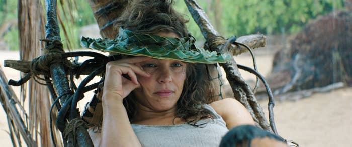 Rachel McAdams relaxing on a beach, wearing a hat made of woven leaves, with a thoughtful expression in a scene from Send Help