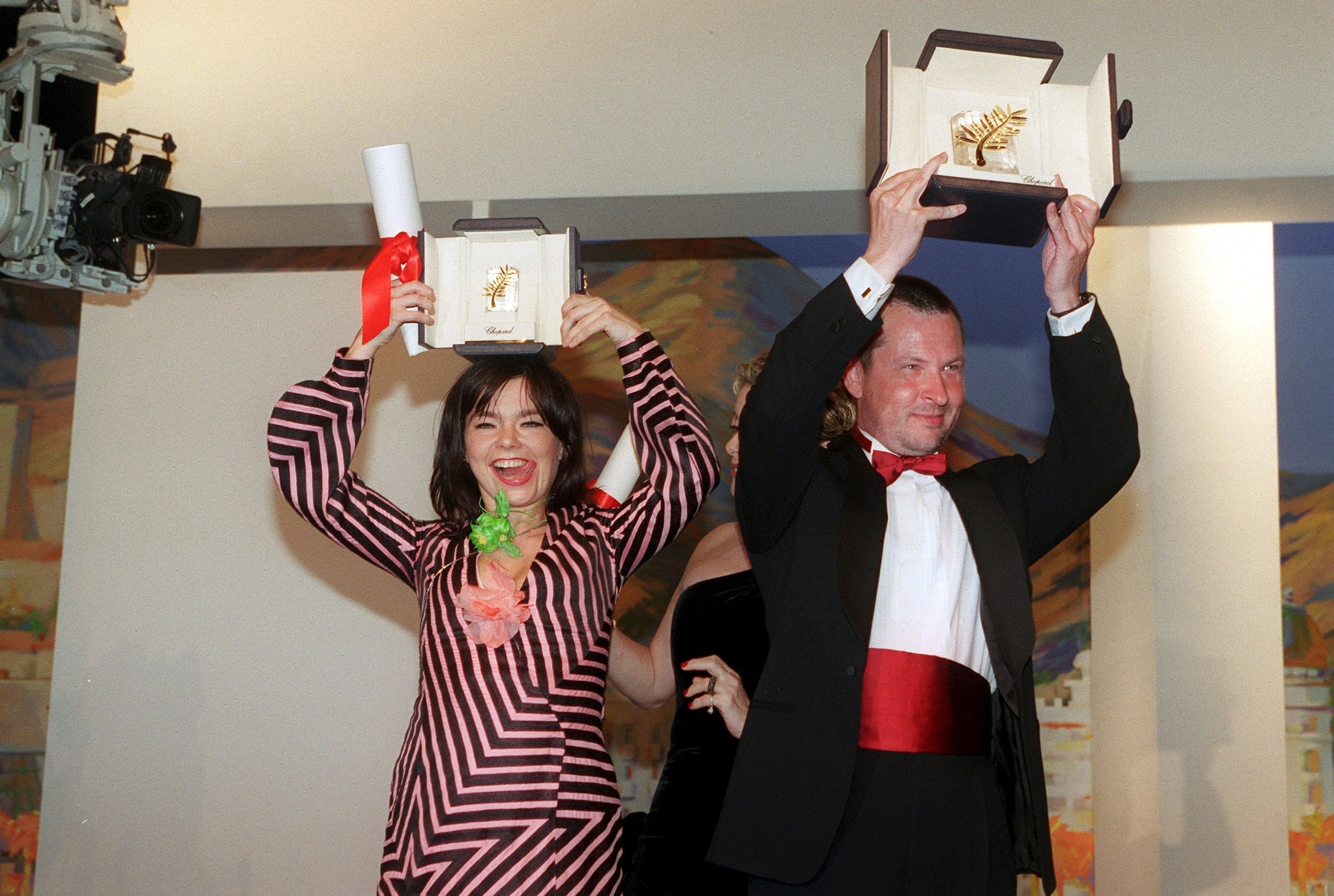 Two radical   successful  ceremonial  attire observe  with awards held high. The pistillate   wears a patterned dress, the antheral   a suit   with a reddish  bow tie