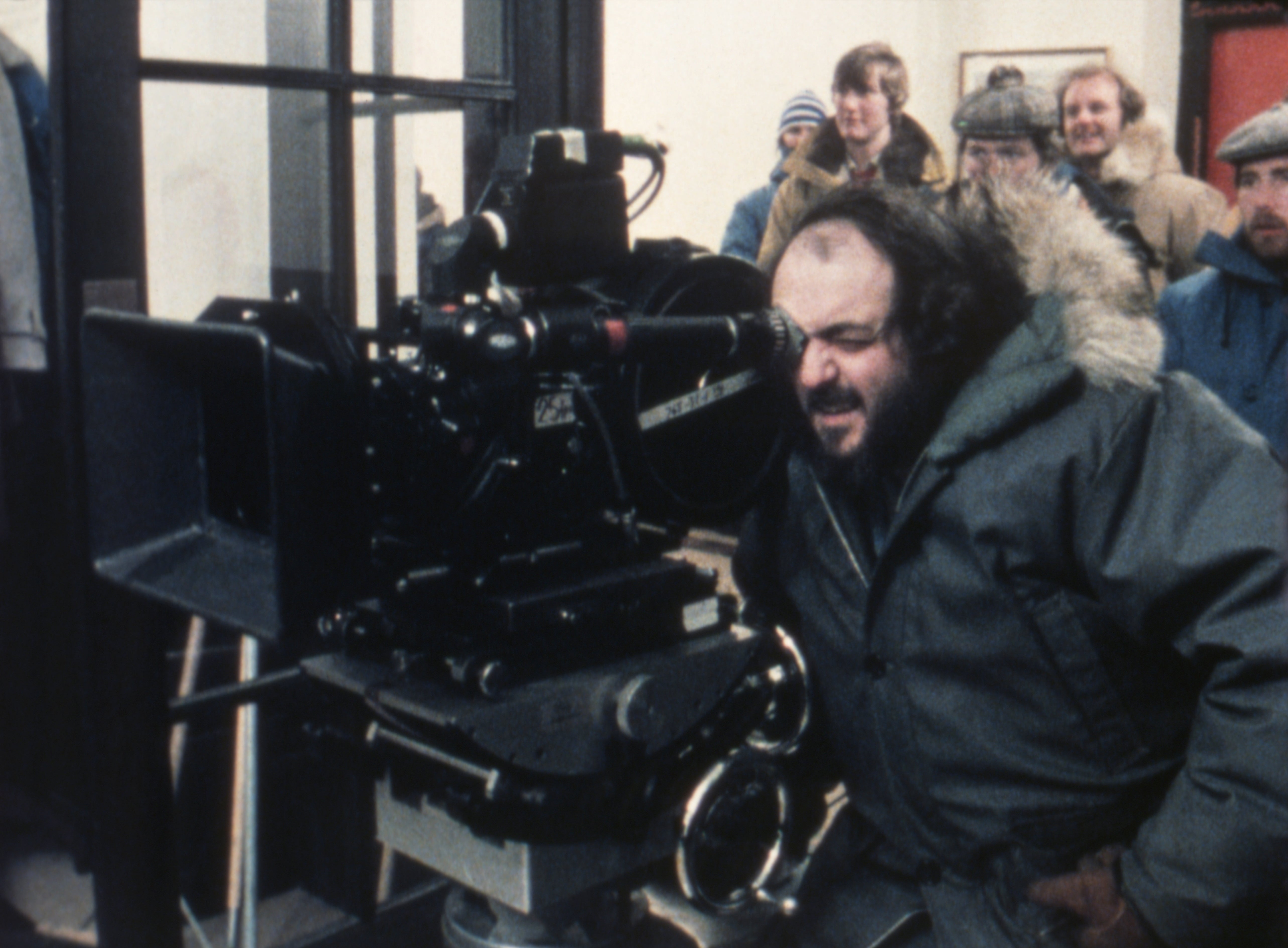 Person looks done  a movie  camera connected  set, surrounded by unit  members wearing wintertime  clothing