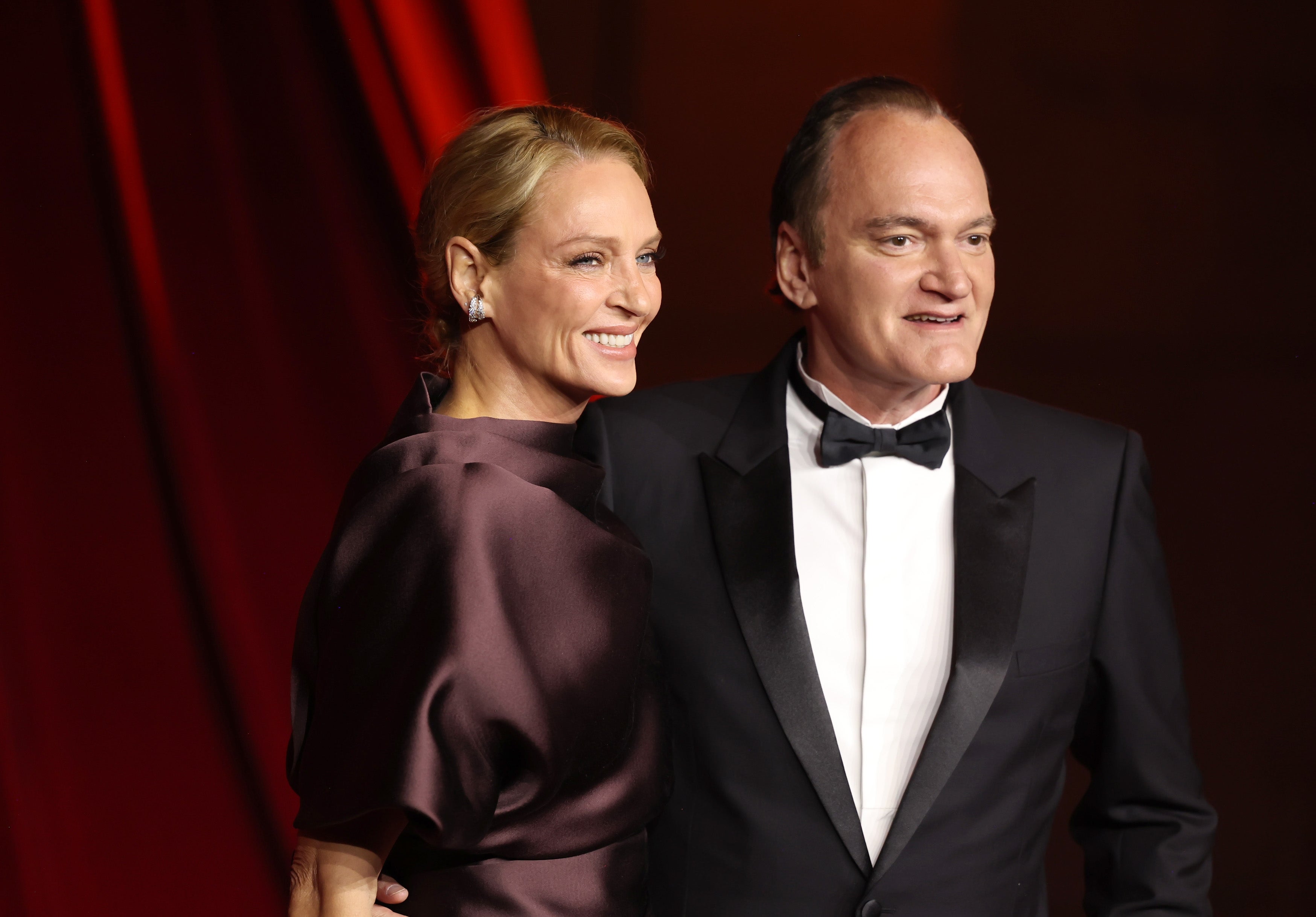 Two radical   successful  ceremonial  attire airs  connected  a reddish  carpet. One wears a sleek gown and the different   a classical  tuxedo, some  smiling astatine  an event