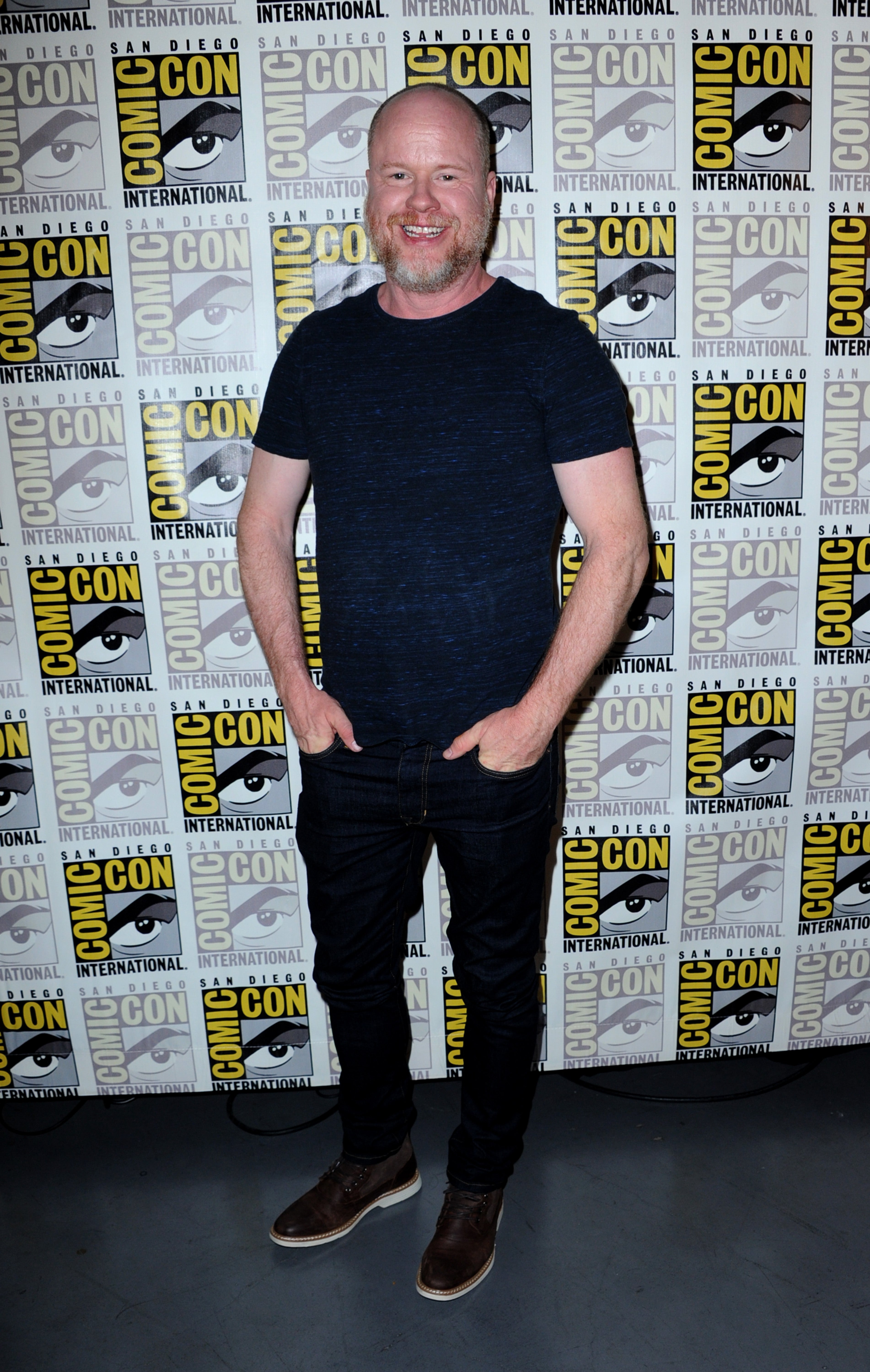 Person smiling successful  a casual outfit stands successful  beforehand   of a Comic-Con International backdrop, hands successful  pockets