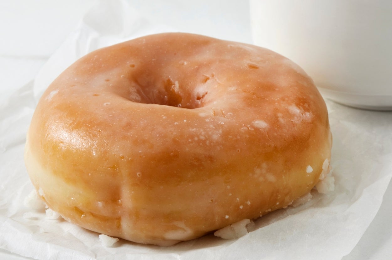 A glazed doughnut on a piece of wax paper next to a white cup