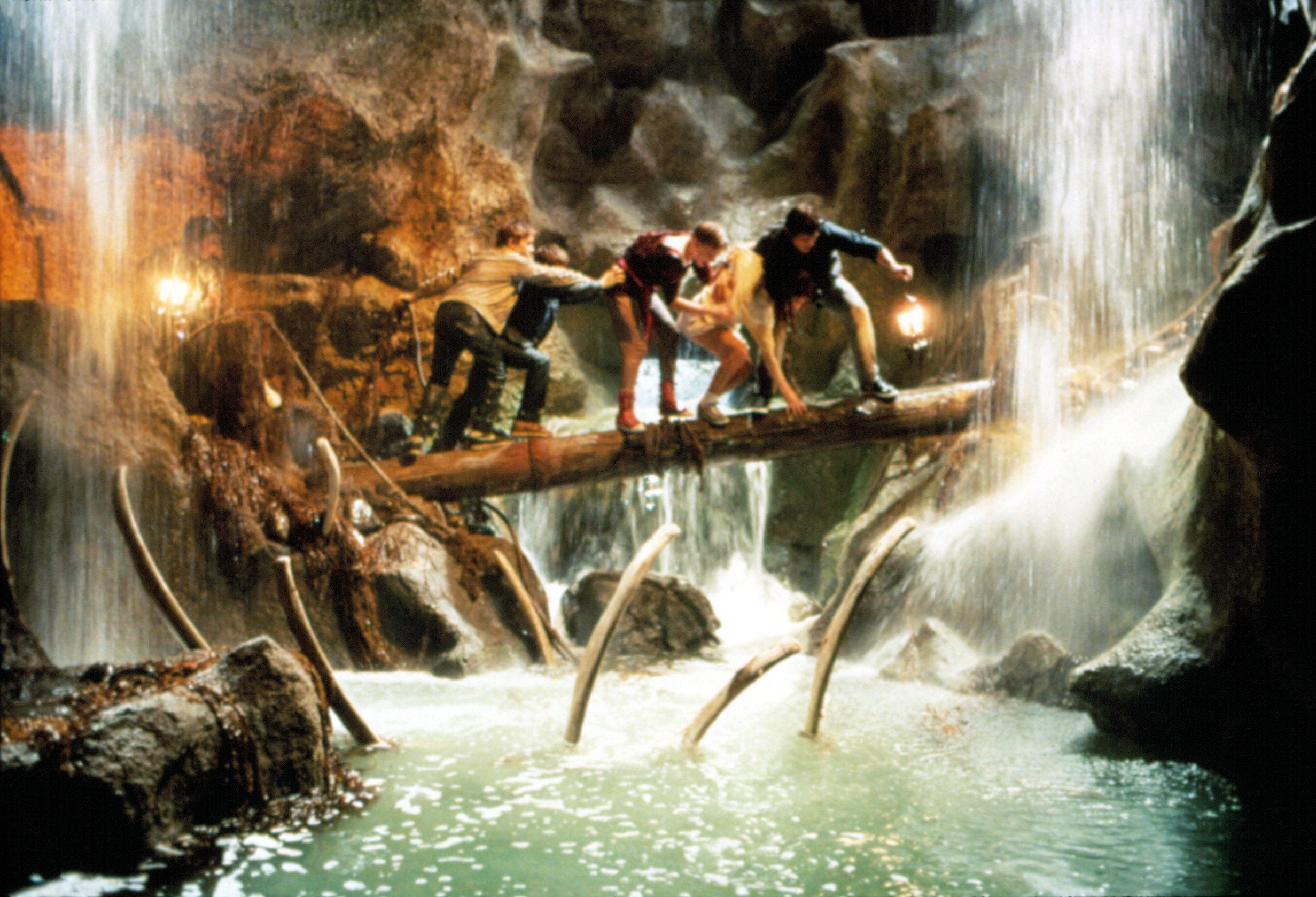 Group of radical cautiously crossing a log span implicit a cave watercourse with waterfalls and stalagmites