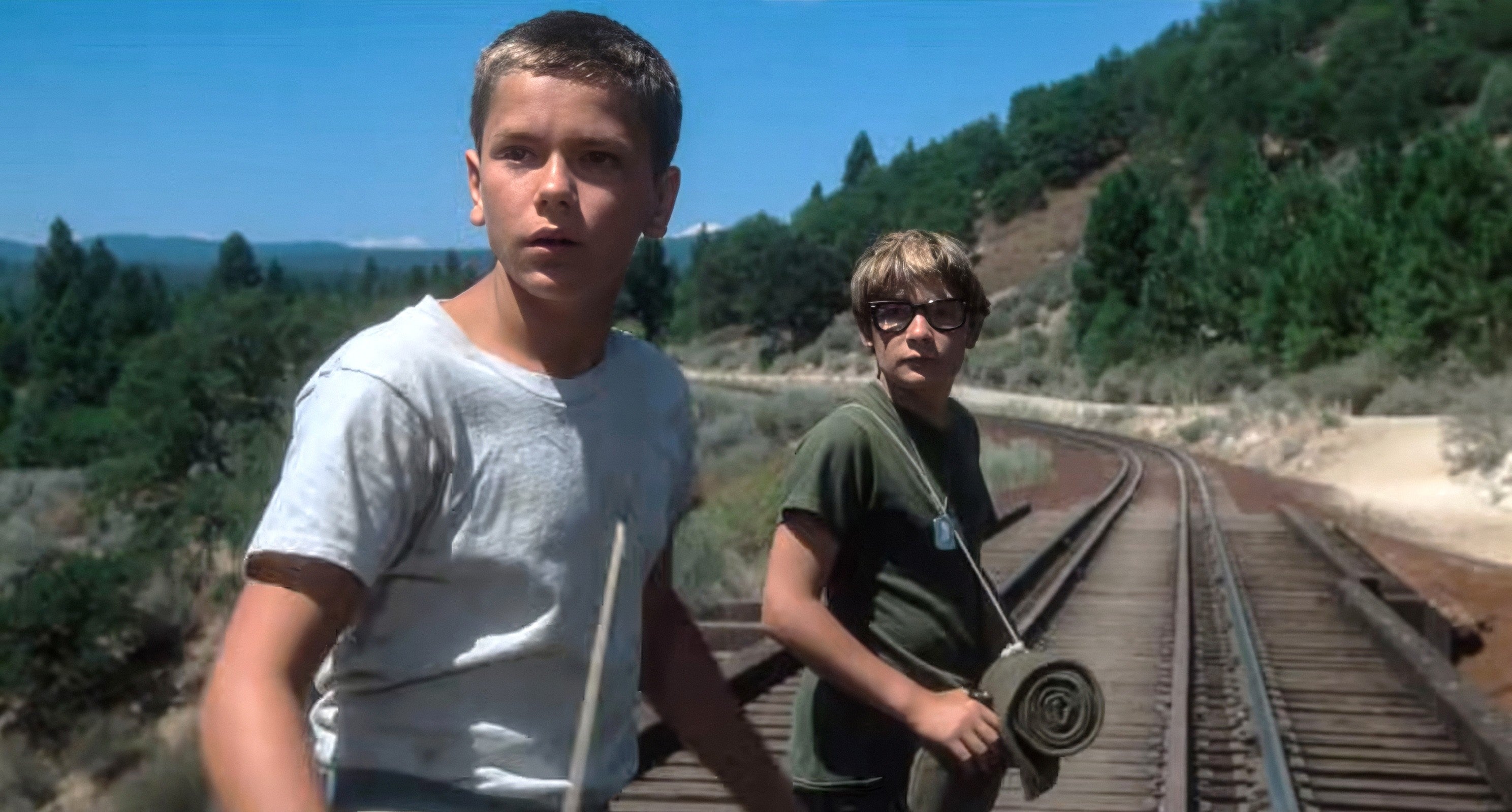 Two young boys basal connected bid tracks successful a forested area, looking concerned. One holds a stick, portion the different carries a rolled-up mat
