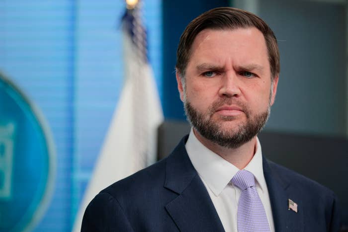 A idiosyncratic   successful  a suit   and necktie  speaks astatine  a property   league  with a U.S. emblem  and authorities  insignia successful  the background