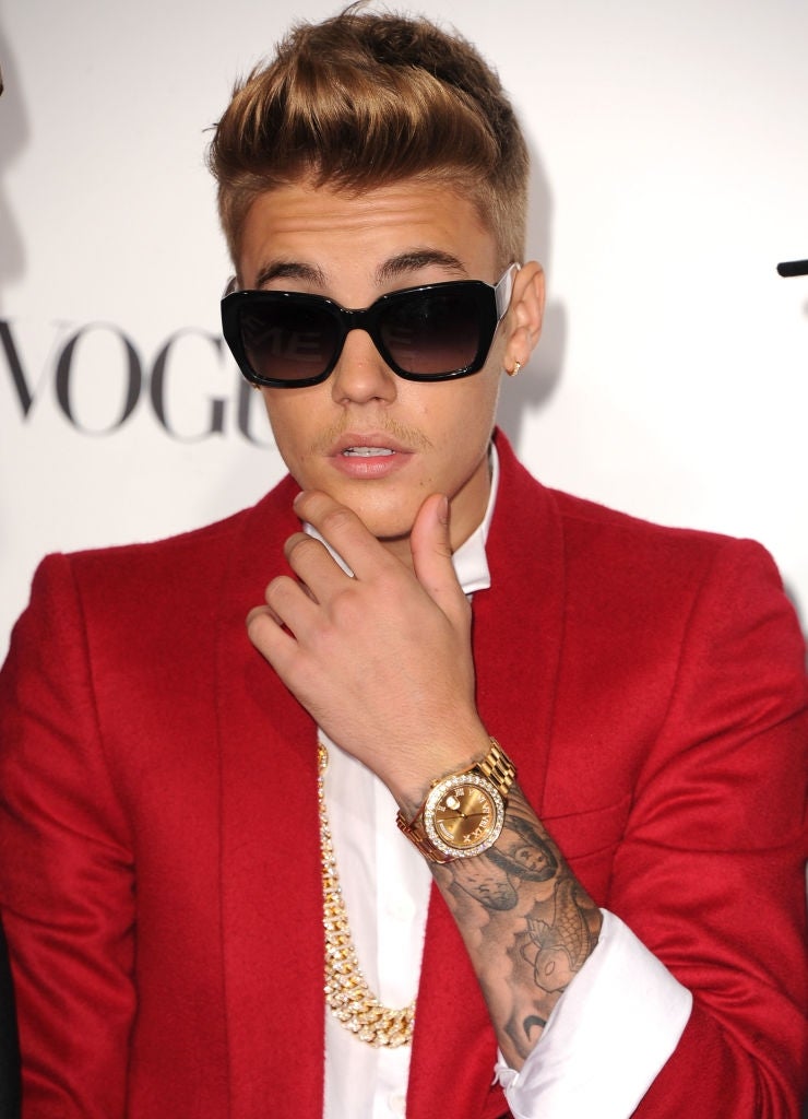 Young antheral successful a crisp suit with sunglasses, wearing golden chains and a watch, posing thoughtfully
