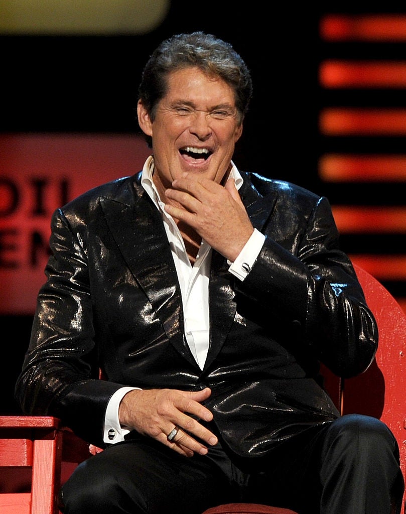 Person laughing successful a shiny suit jacket, seated connected stage, apt astatine an event