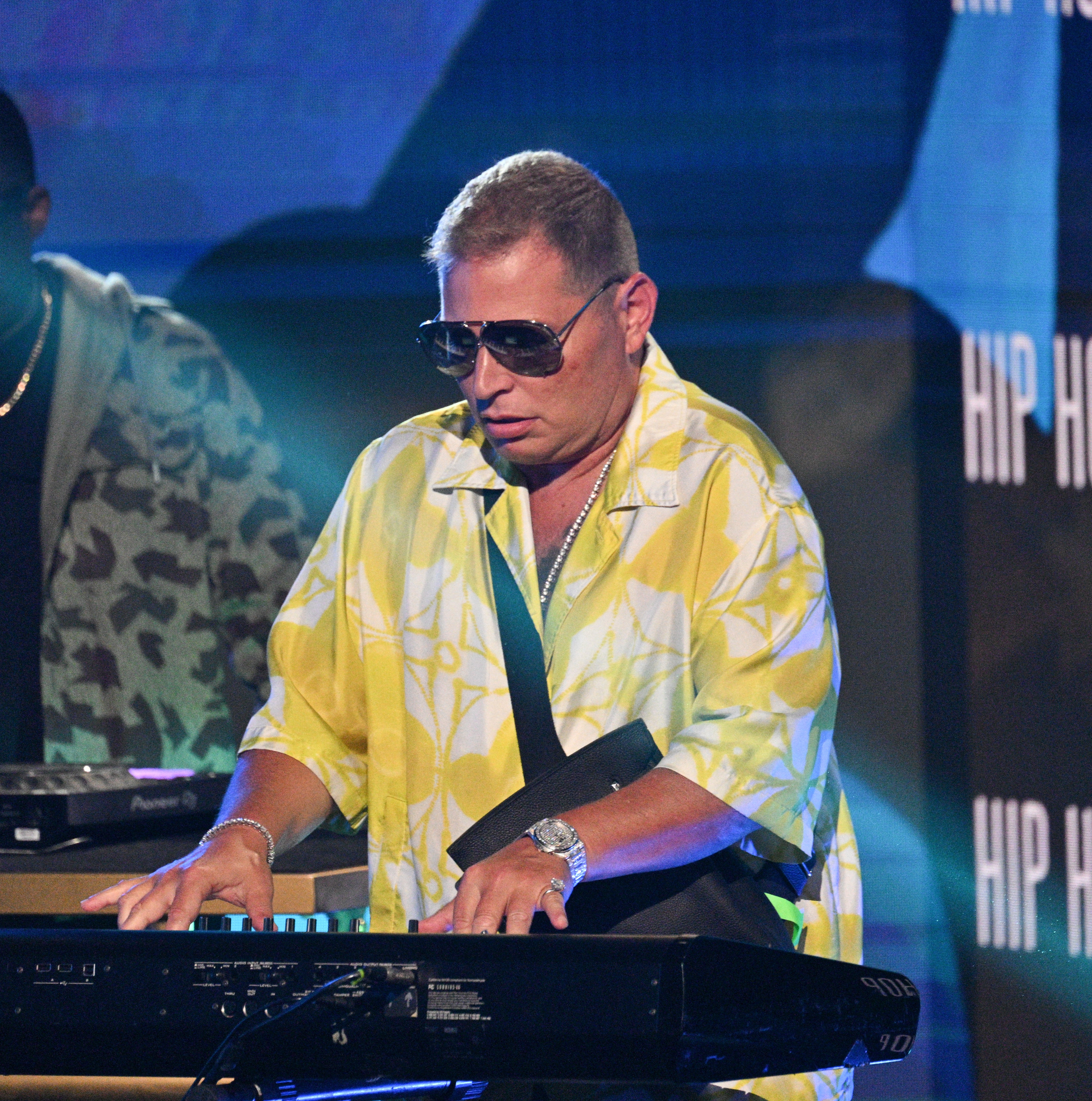Scott Storch playing keyboard on stage, wearing sunglasses and a patterned shirt